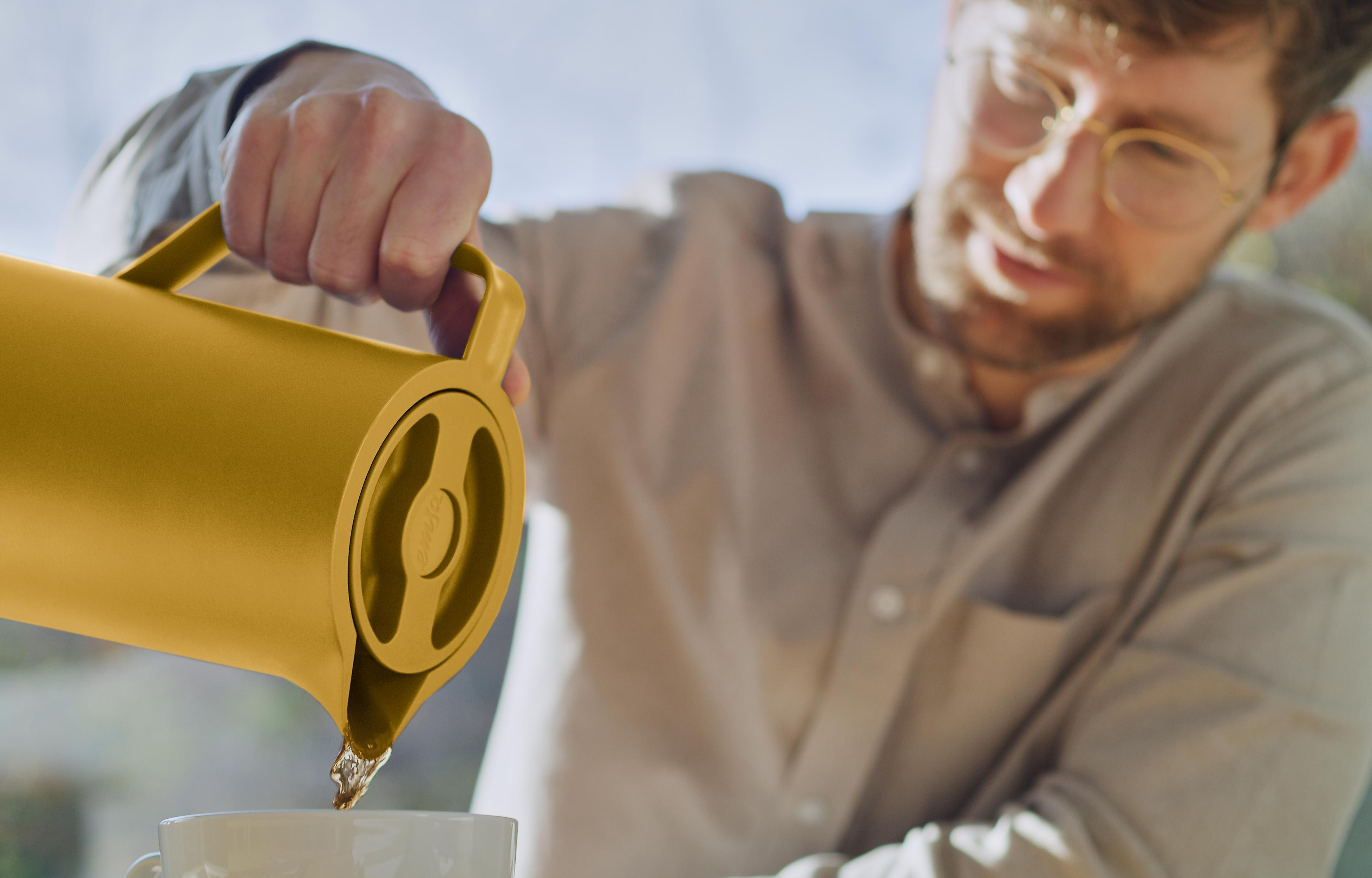 Ein Mann gießt Flüssigkeit aus einer gelben Thermoskanne in eine Tasse.