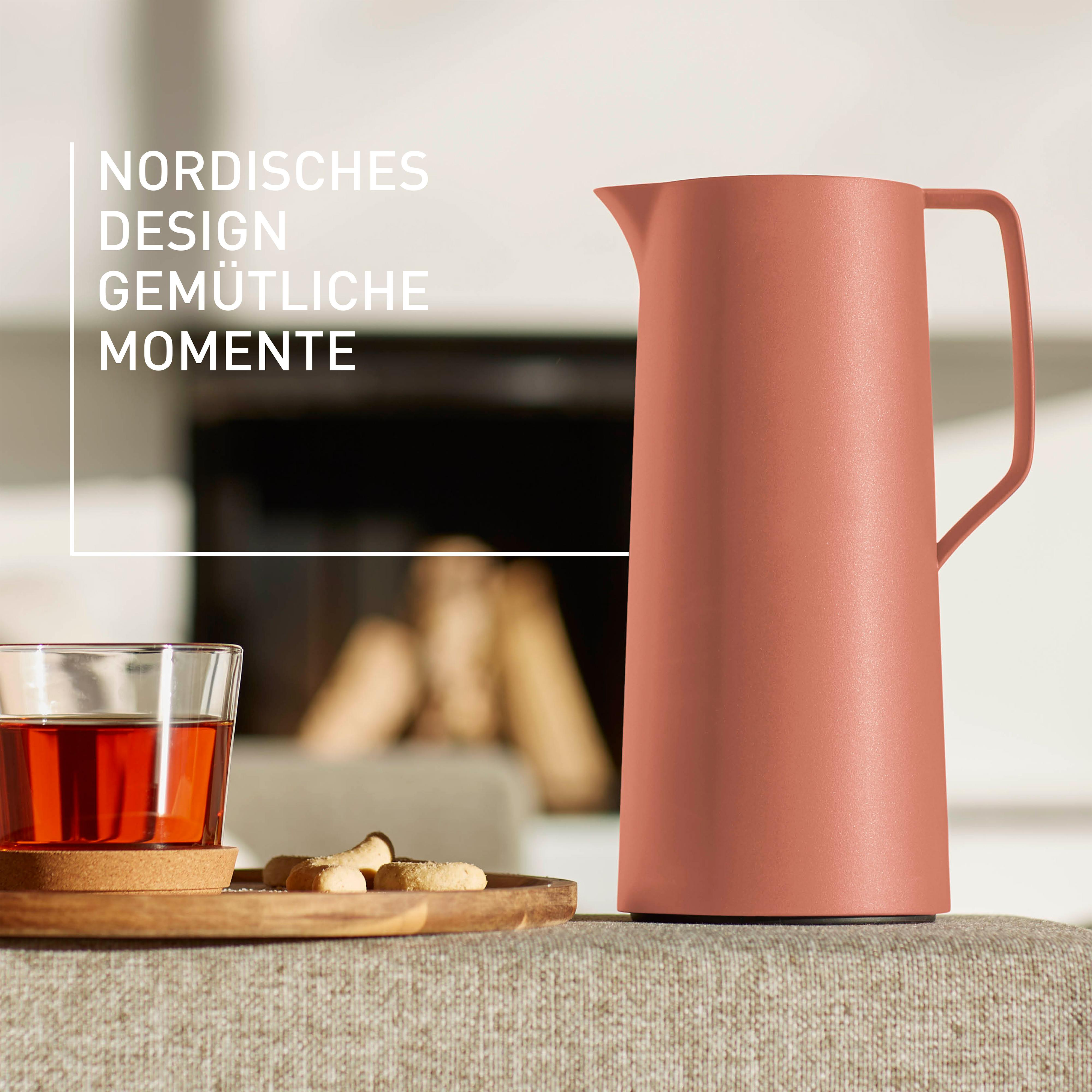 Eine terrakottafarbene Kanne und ein Glas mit Tee auf einem Holztablett, ein Kamin im Hintergrund.