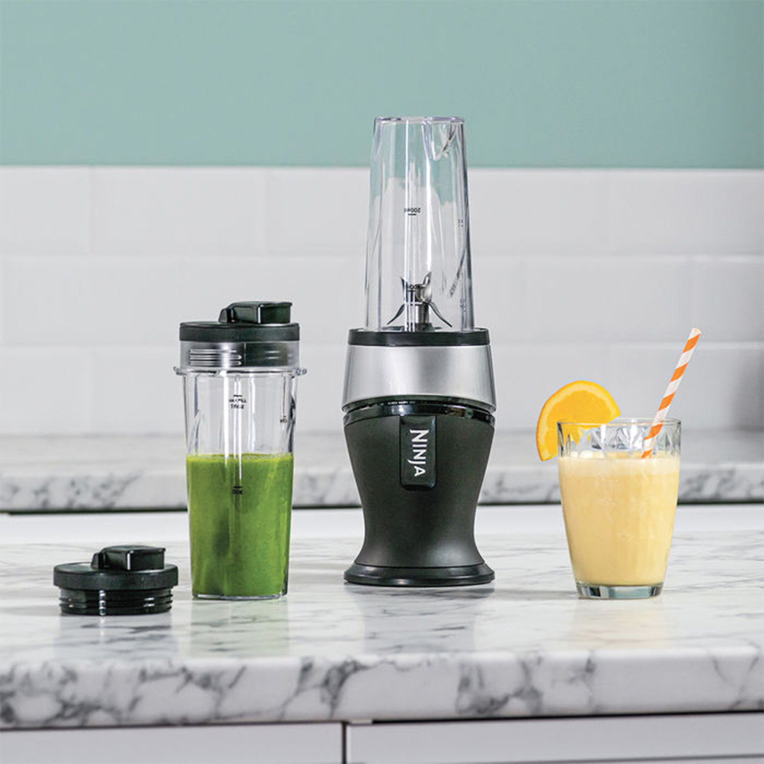 Frullatore con due bicchieri, uno con liquido verde, e un bicchiere di succo d'arancia con cannuccia.