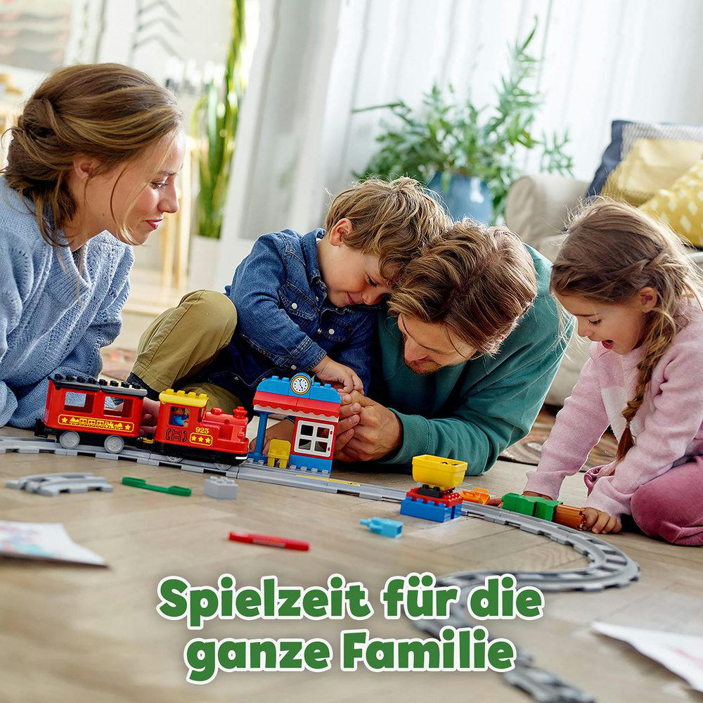 Familie spielt mit Lego. Eltern und Kinder bauen gemeinsam eine Eisenbahn auf Holzboden.