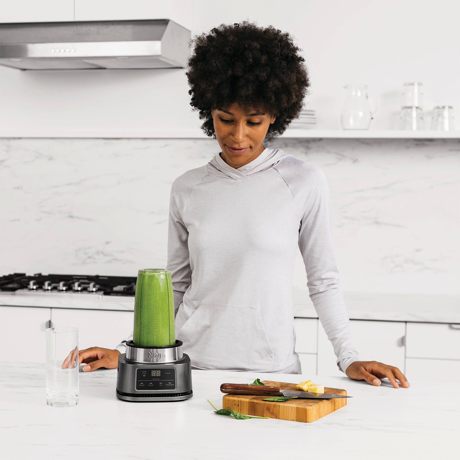 Donna in cucina con frullato verde nel frullatore. Bancone in legno. Sfondo bianco.