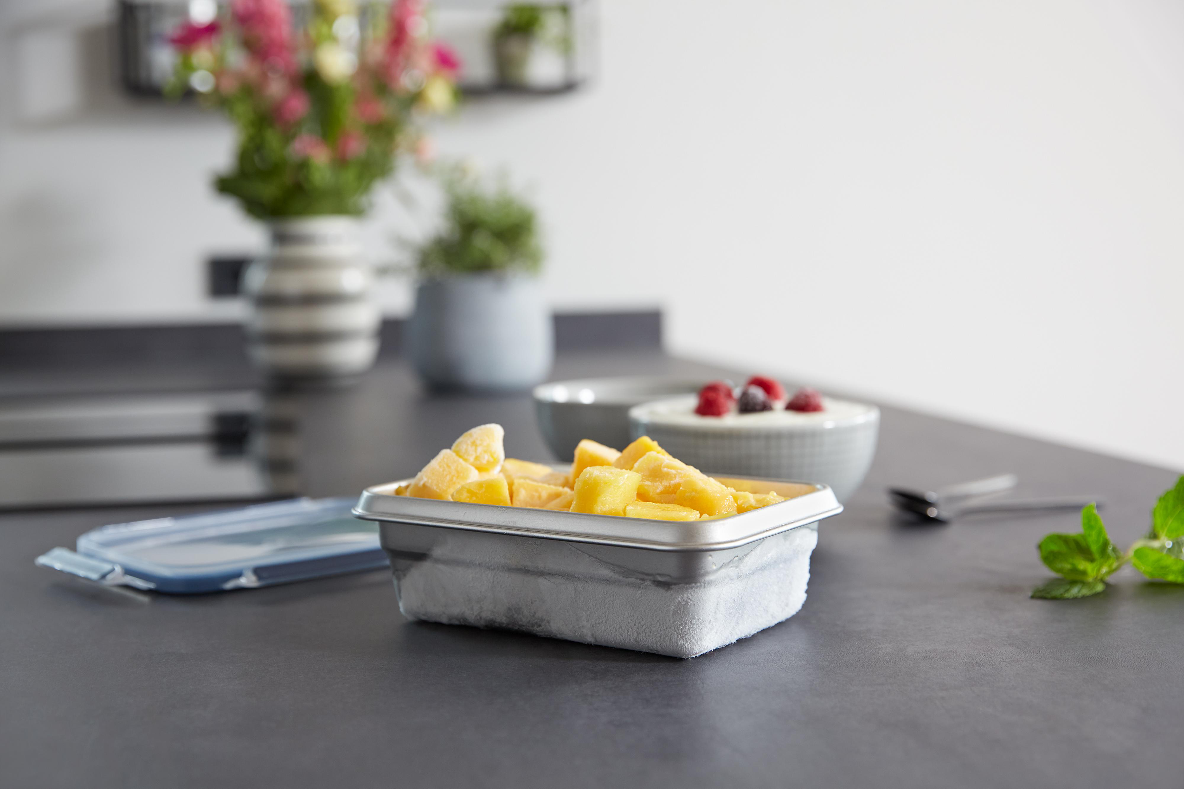 Ein Behälter mit geschnittenen Mangos auf einer Küchentheke. Es gibt auch Schüsseln und Blumen.