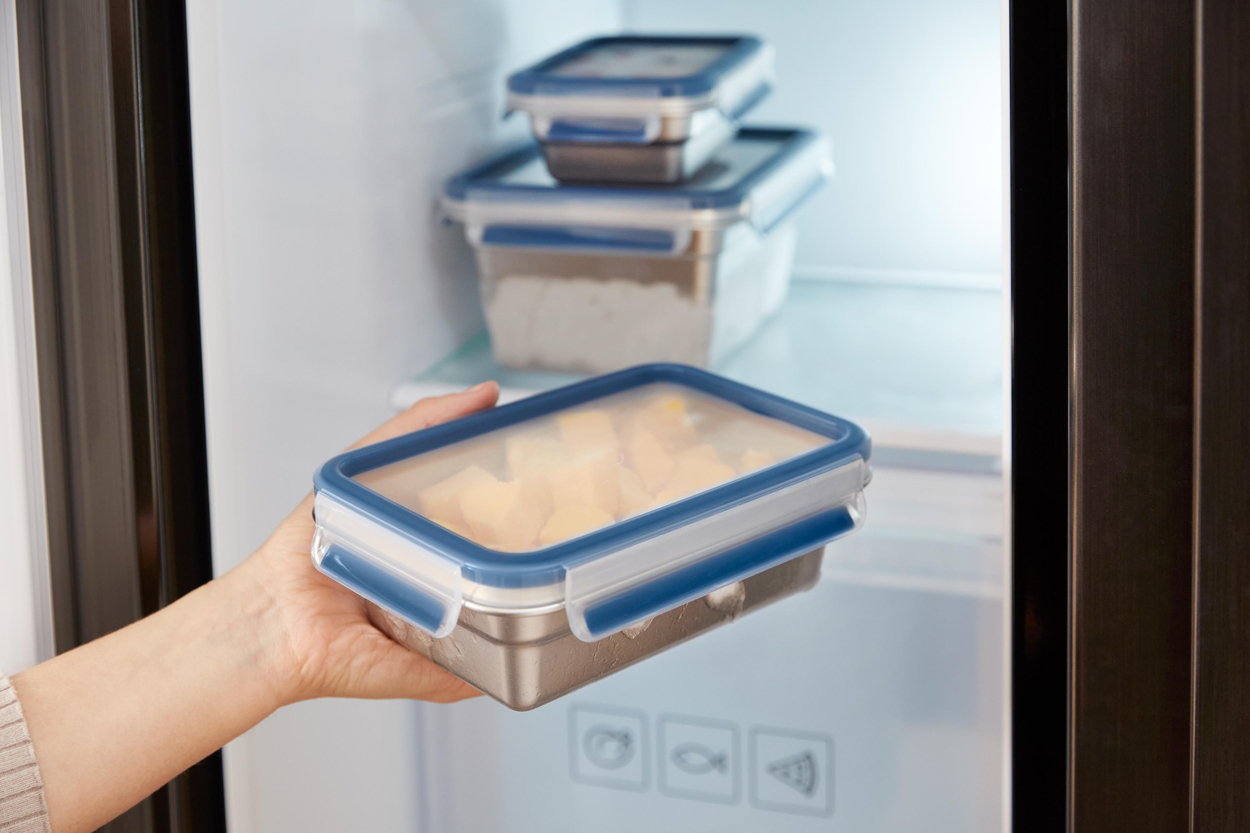 Eine Hand, die einen Behälter mit Essen in einen Kühlschrank stellt, in dem sich weitere Behälter befinden.