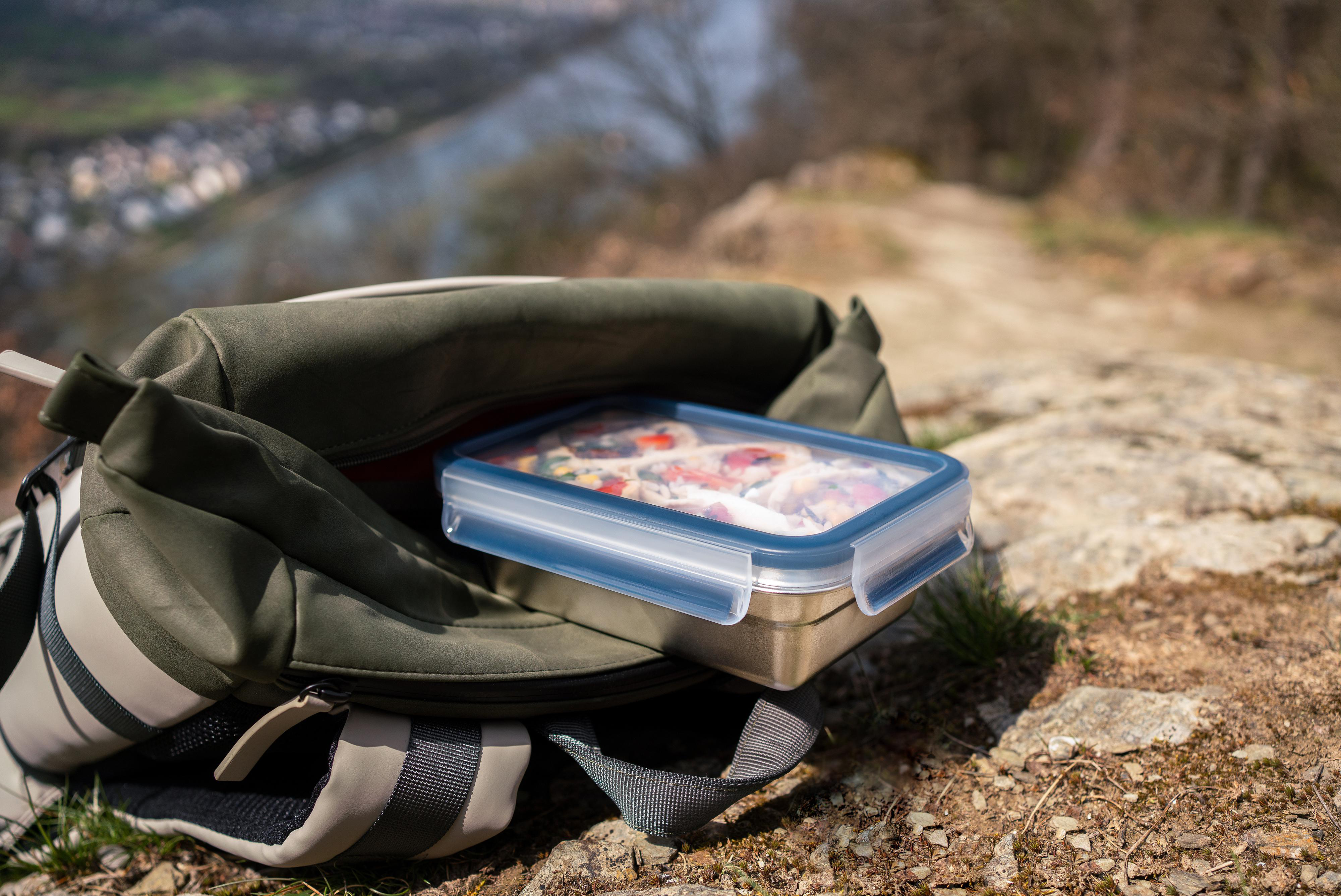 Lunchbox in offenem Rucksack auf Hügel mit Blick auf Fluss.