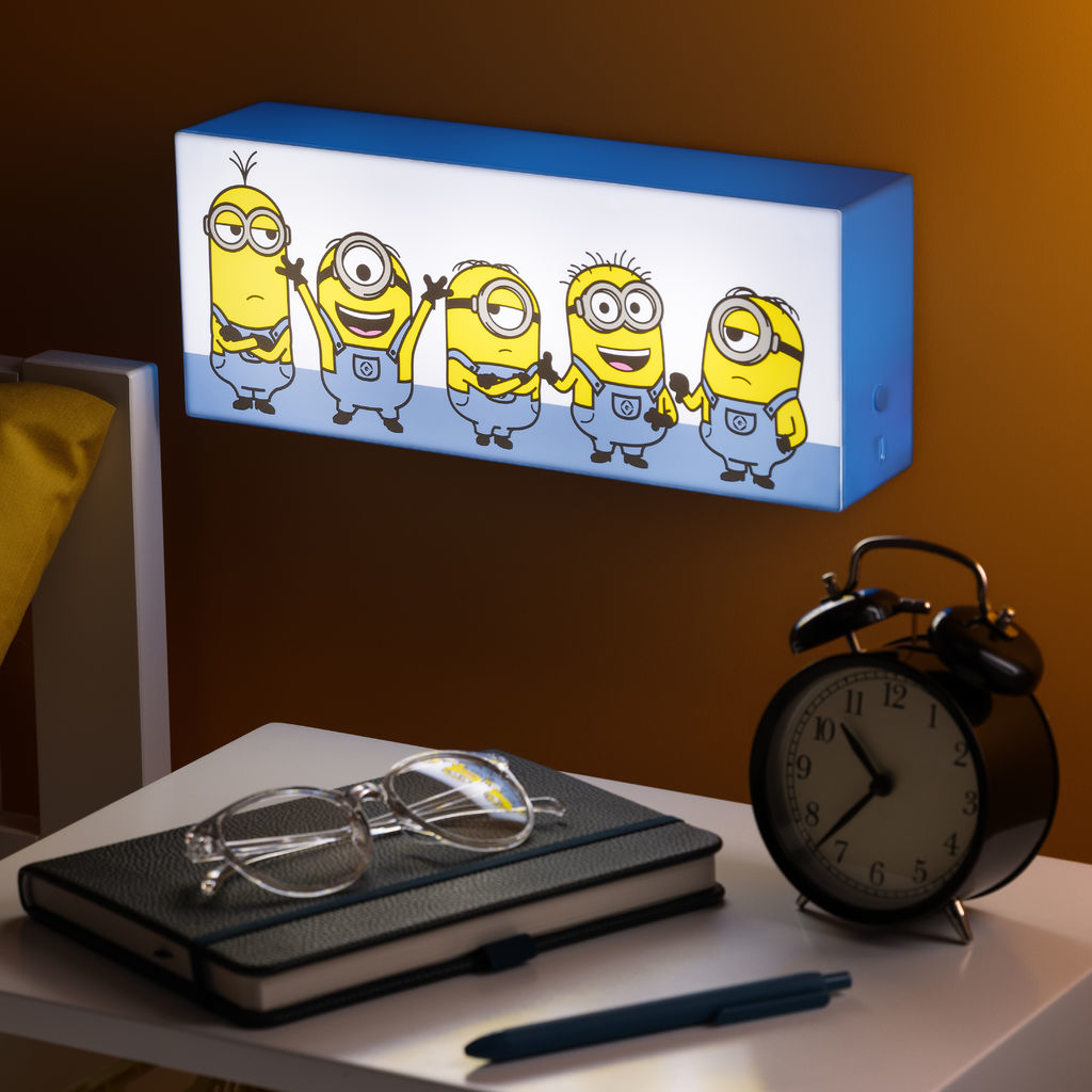 Minions témájú éjszakai fény egy éjjeliszekrény felett, ébresztőórával, szemüveggel, noteszfüzettel és tollal.