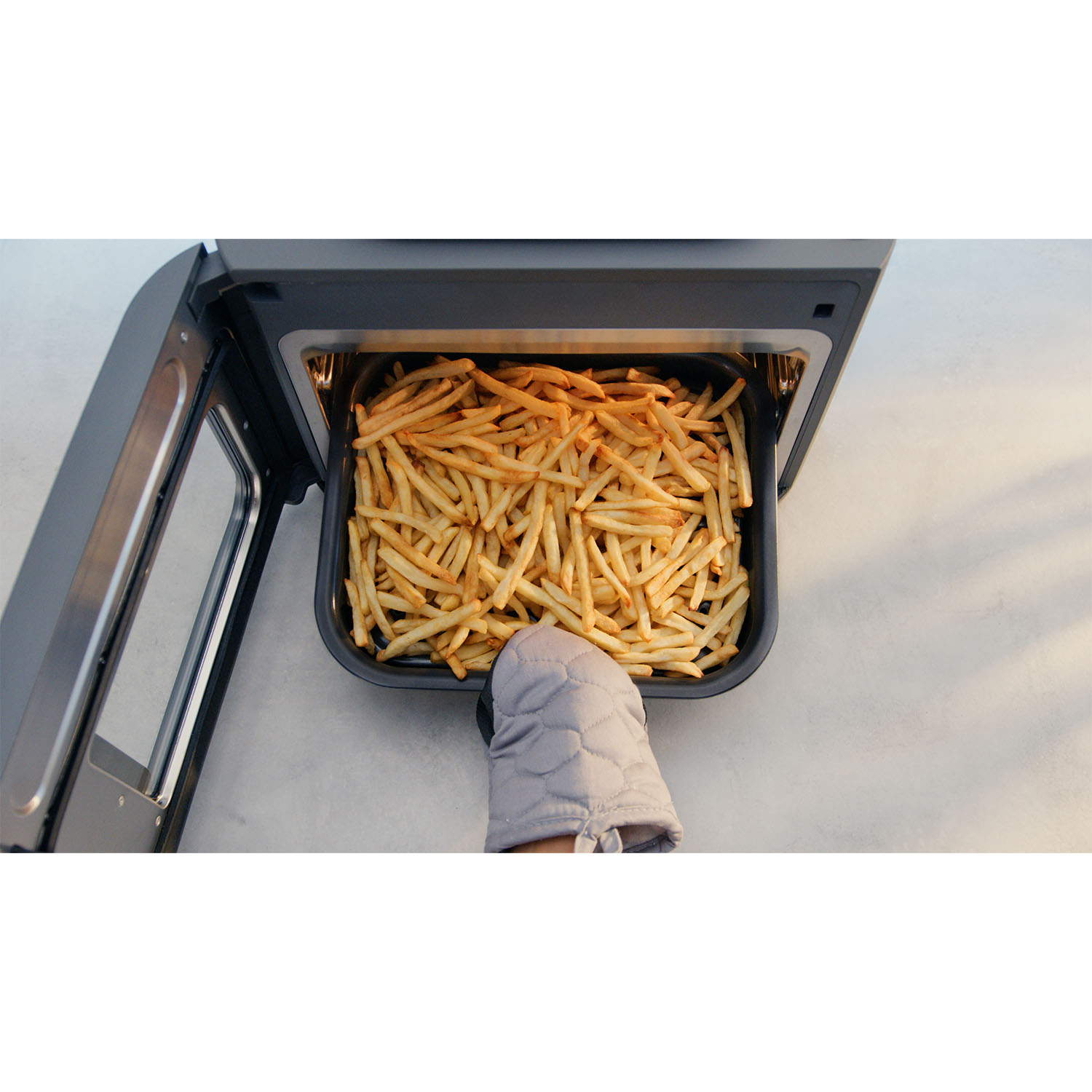 Una friggitrice ad aria con un vassoio di patatine fritte rimosso da una mano guantata.
