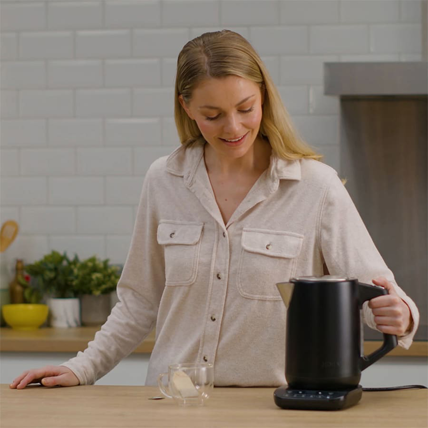 Donna con un bollitore nero e un bicchiere di tè, in un ambiente cucina.