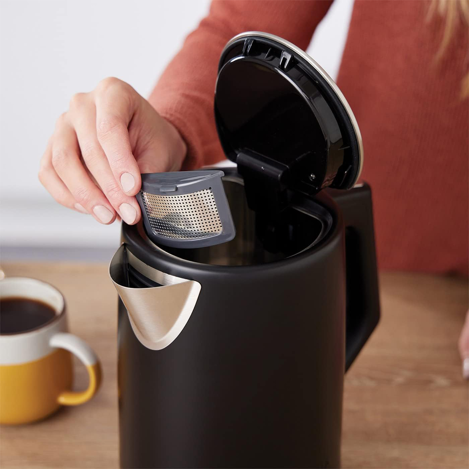 Persona che inserisce un infusore per tè in un bollitore nero.