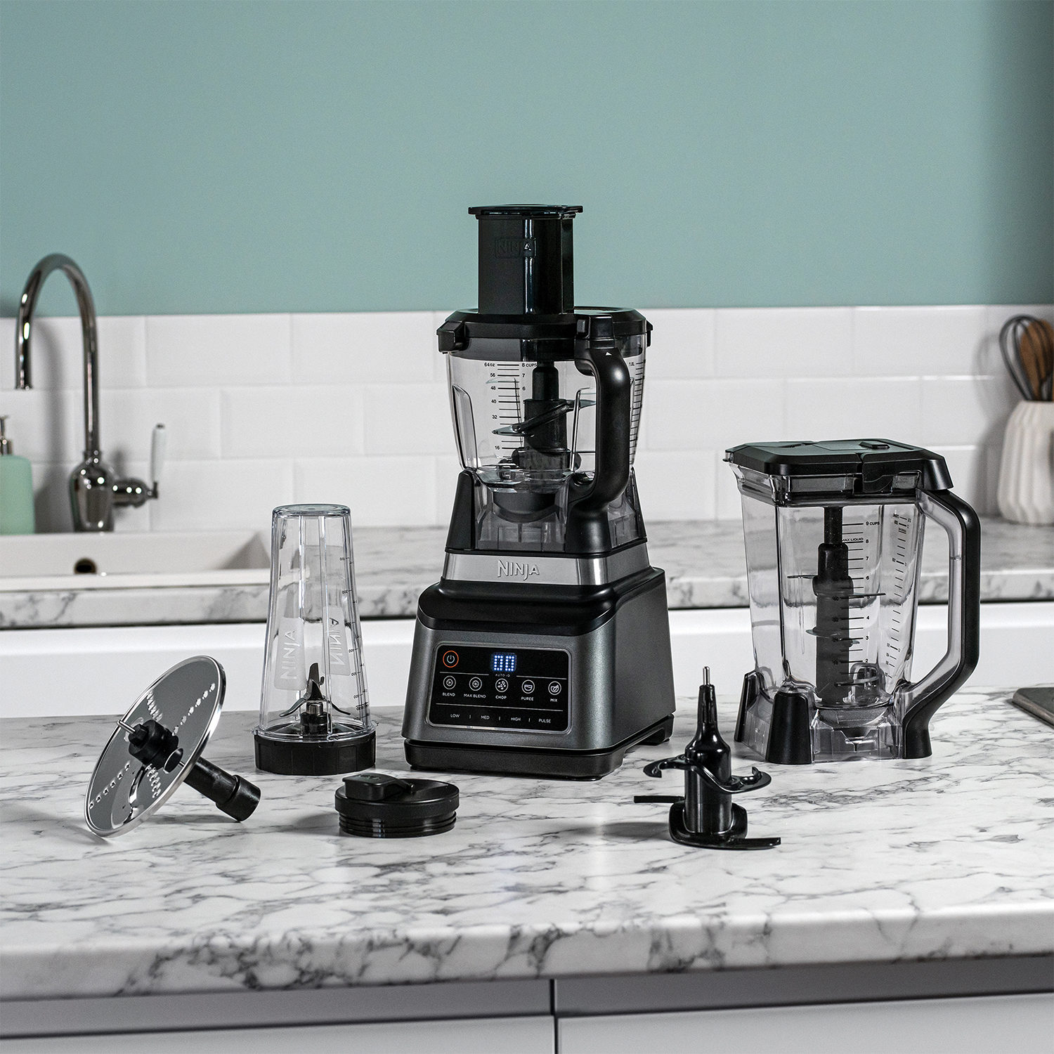 Robot da cucina Ninja con varie parti su piano di lavoro in marmo e sfondo turchese.