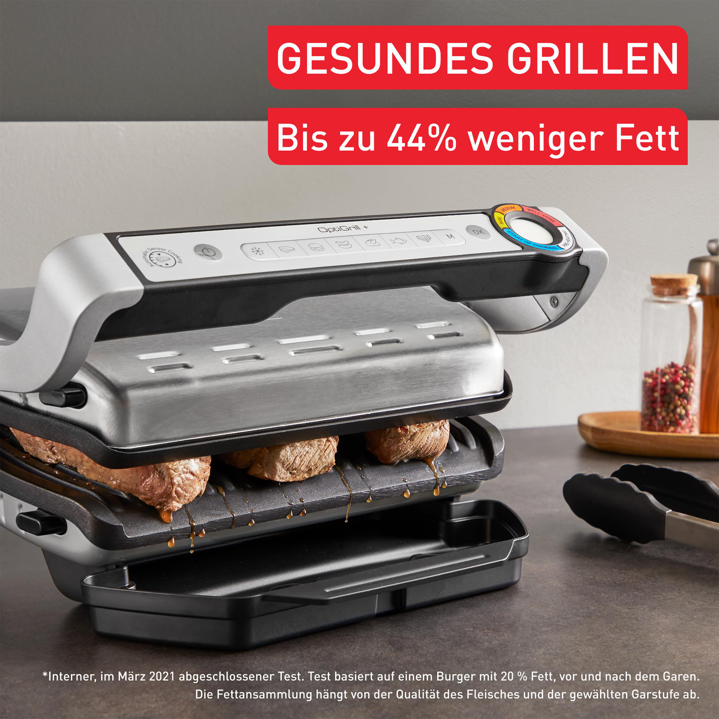 Grill mit Fleisch darauf. Text besagt gesundes Grillen und bis zu 44 % weniger Fett. Schwarze Zange daneben.