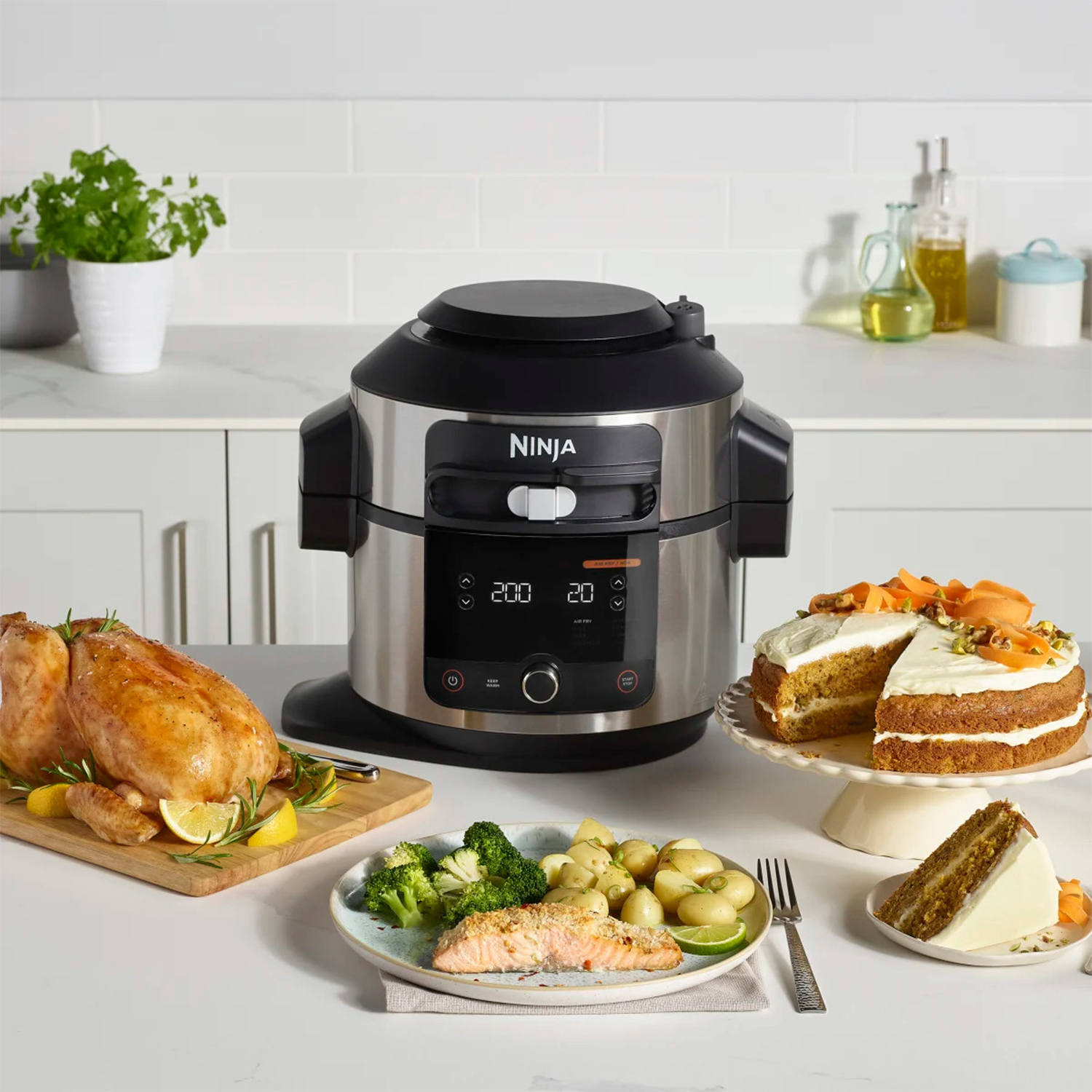 Un multicooker Ninja con pollo arrosto, torta e altri piatti su un tavolo in una cucina.