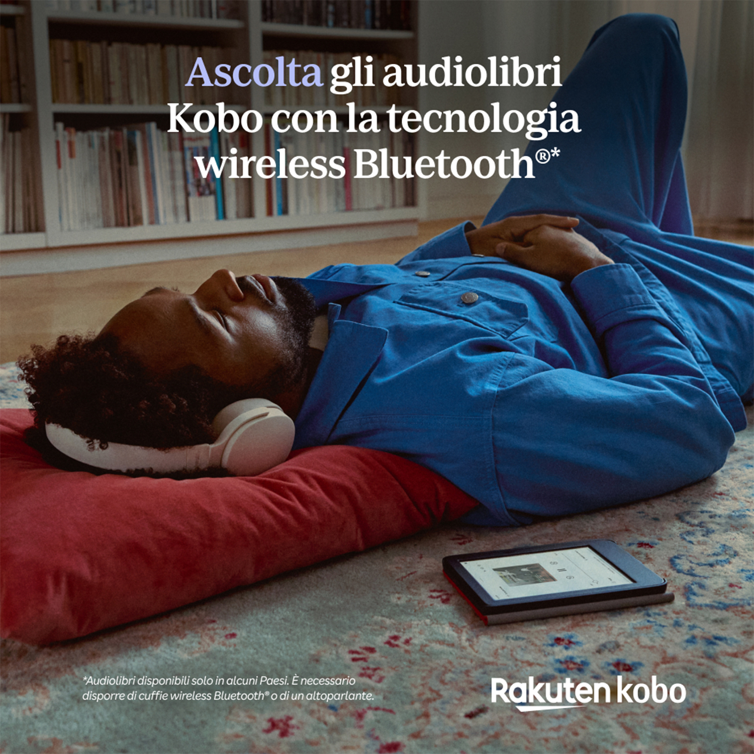 Uomo che ascolta audiolibri con Kobo, sdraiato su un tappeto con un libro.
