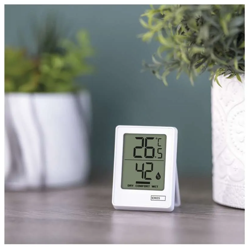Egy fehér digitális hőmérő, 26,5°C-t és 42%-ot mutat. Növényekkel körülvéve.