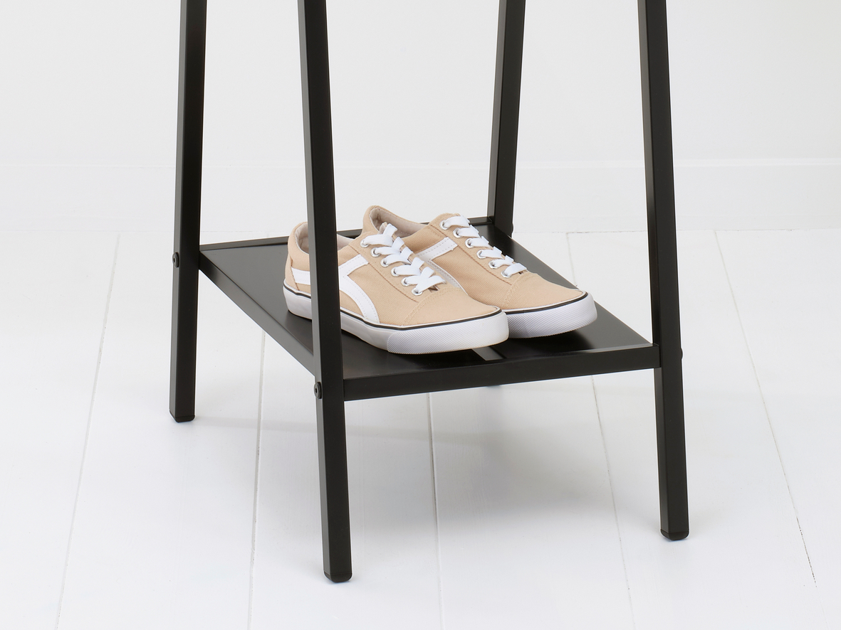 Schuhregal aus schwarzem Metall. Beige Turnschuhe mit weißen Schnürsenkeln auf dem Regal, weißer Boden im Hintergrund.
