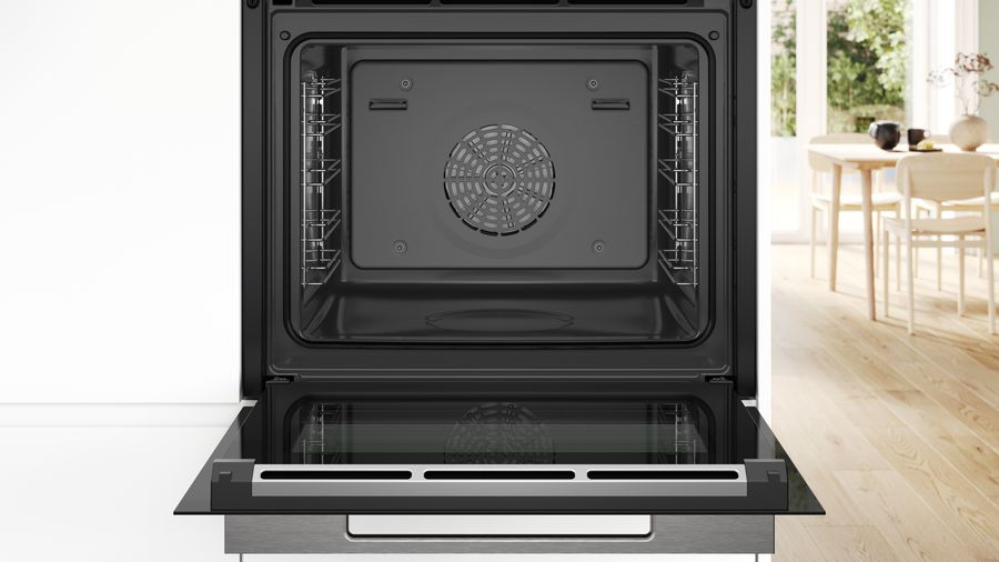 Interior de horno abierto con ventilador y rejillas. El fondo muestra una cocina con mesa y sillas.