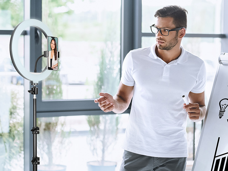 Mężczyzna prezentujący przed tablicą. Smartfon jest na lampie pierścieniowej.