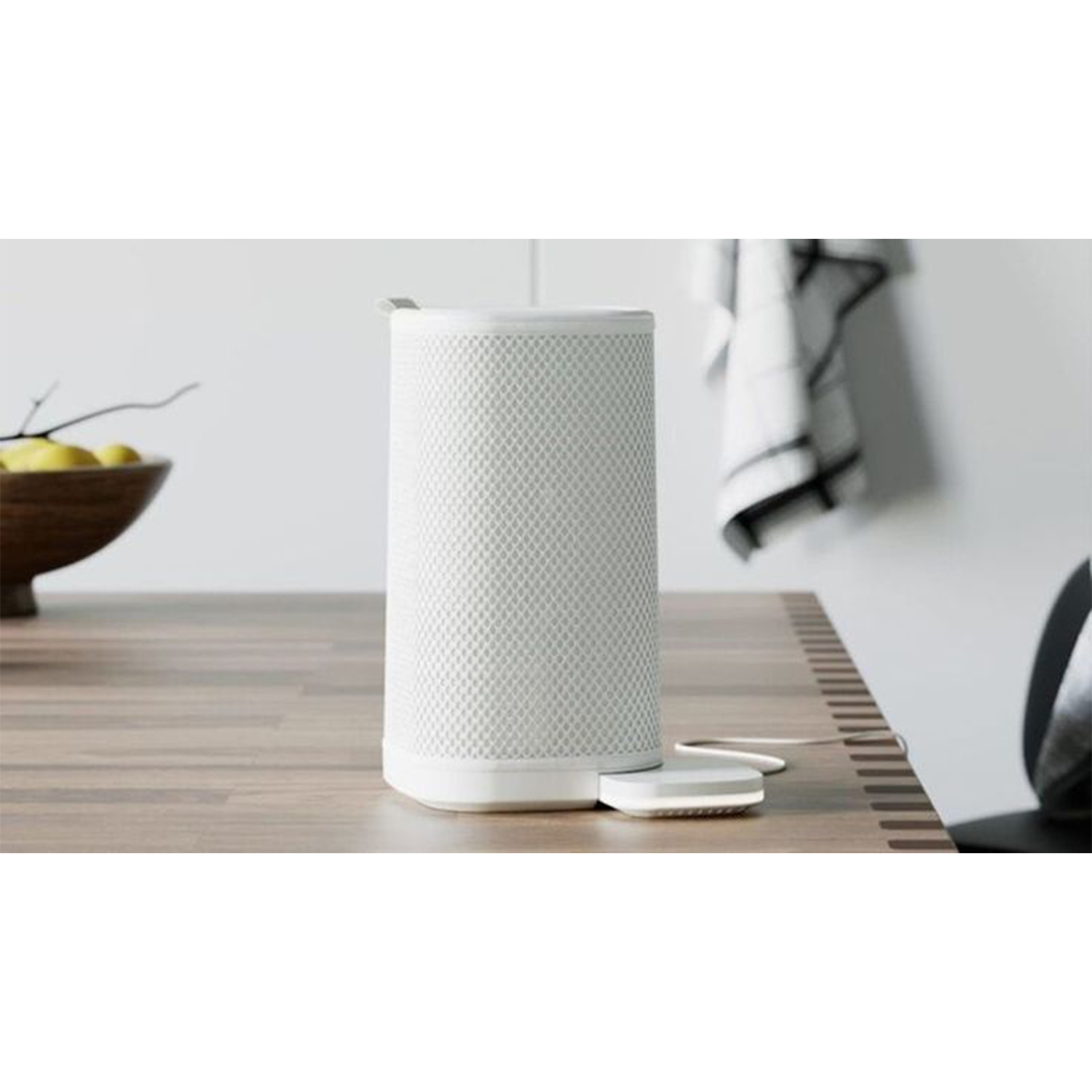 Un altoparlante intelligente bianco con un design a rete è su una superficie di legno con un pad bianco accanto.