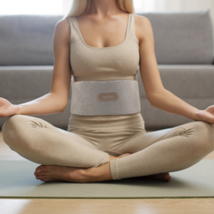 Femme en posture de yoga avec une ceinture chauffante autour de la taille, sur un tapis.