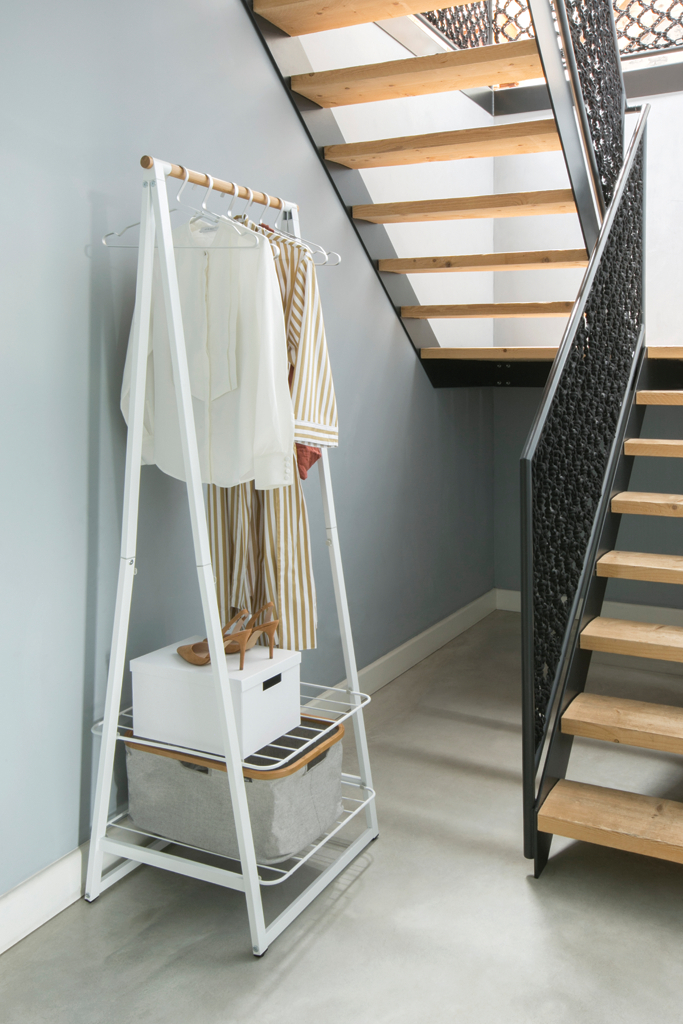 Kleiderständer mit Kleidung, Schuhen und Kisten, neben einer Holztreppe.