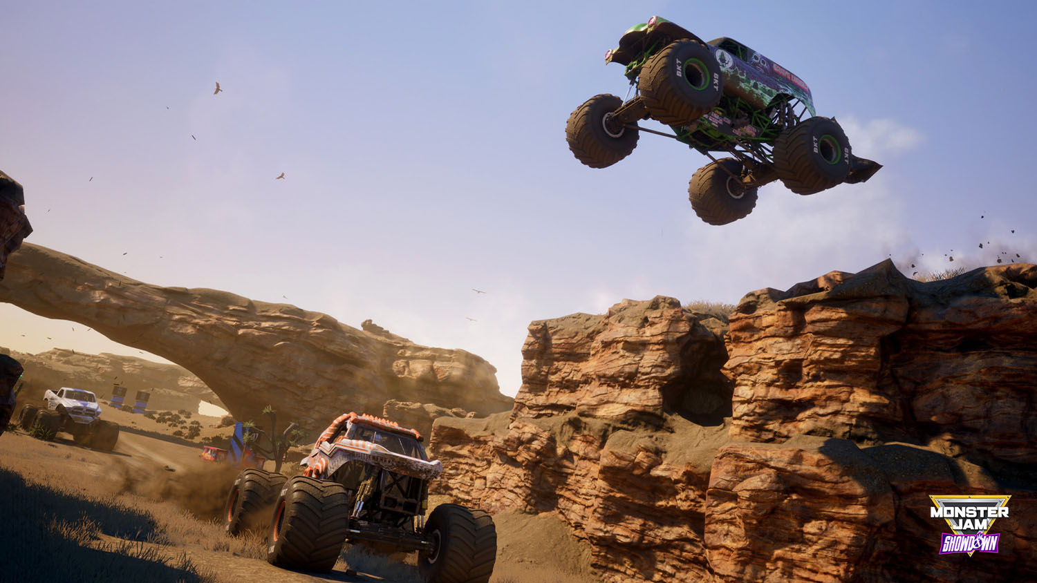 Monster truck en l'air au-dessus d'un paysage désertique avec d'autres camions et ciel bleu.