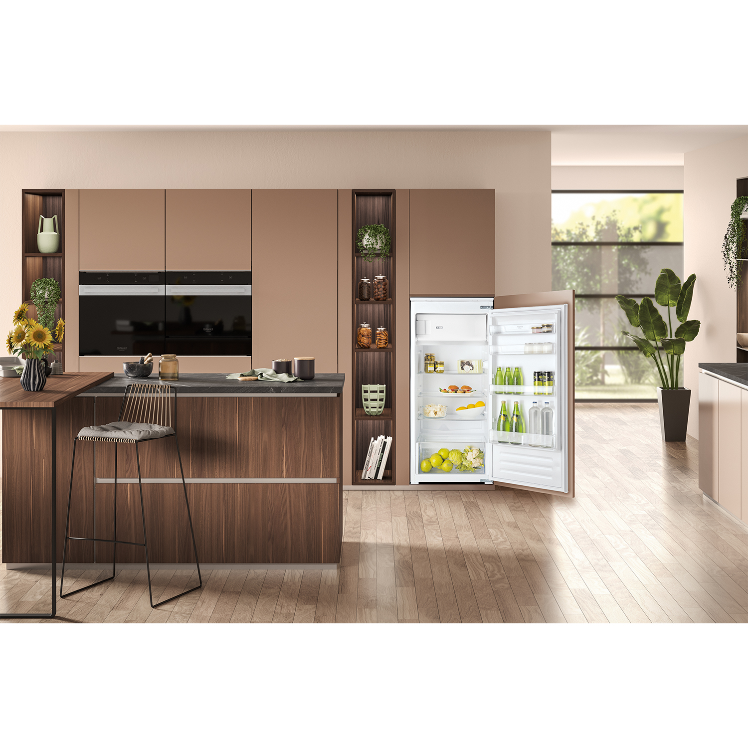 Cucina con frigorifero aperto, isola e forni a incasso. Mobili marroni e pavimenti in legno.