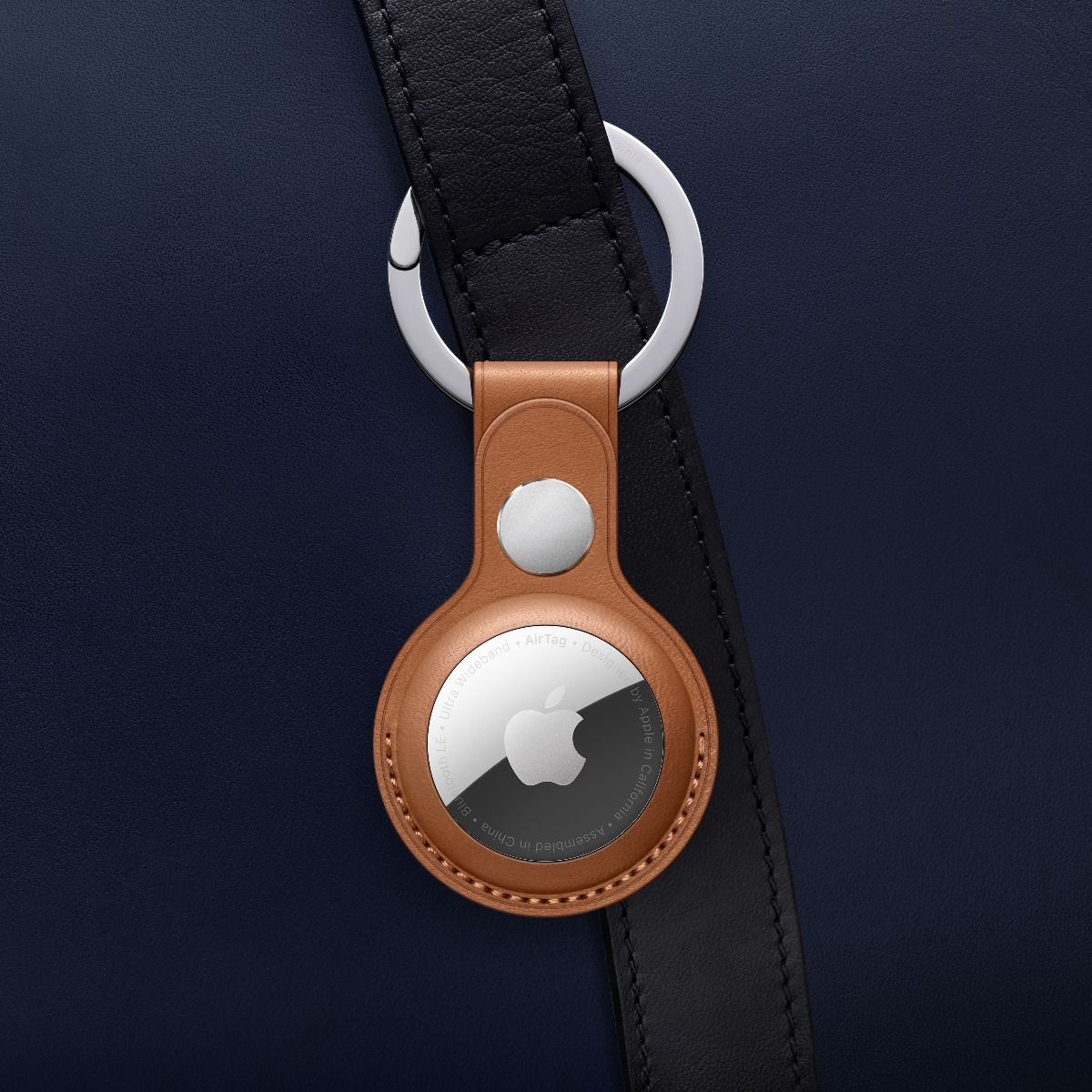 Barna bőr Apple AirTag egy fekete szíjra rögzítve.