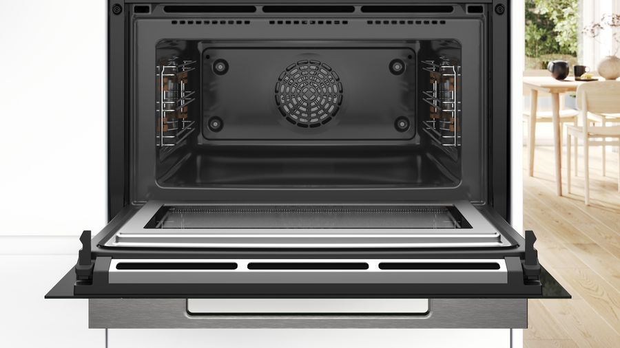Interior del horno con puerta abierta, mostrando rejillas, ventilador y fondo brillante. Cocina blanca.