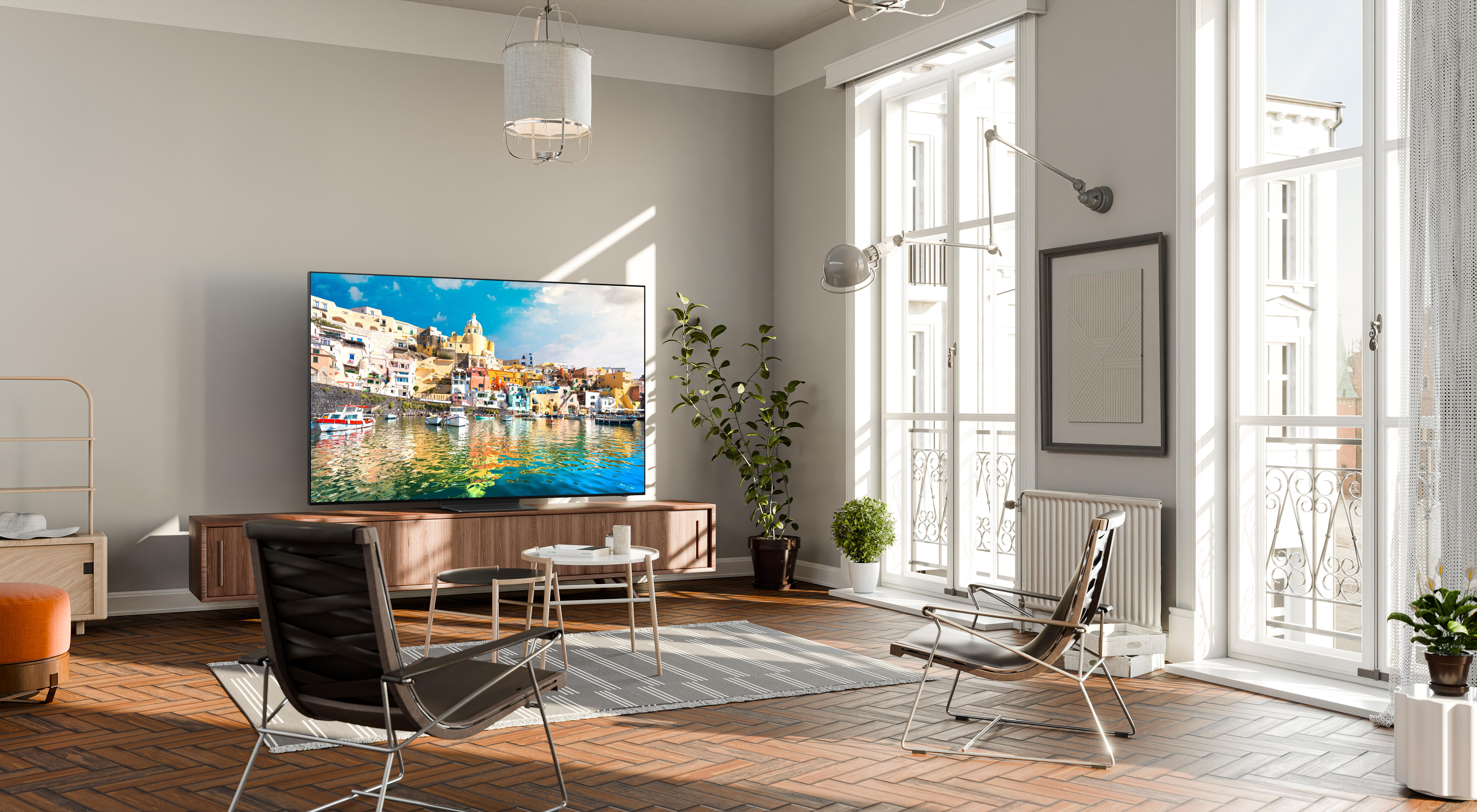 Wohnzimmer mit großem Fernseher, der eine Küstenlandschaft zeigt. Moderne Möbel und große Fenster.