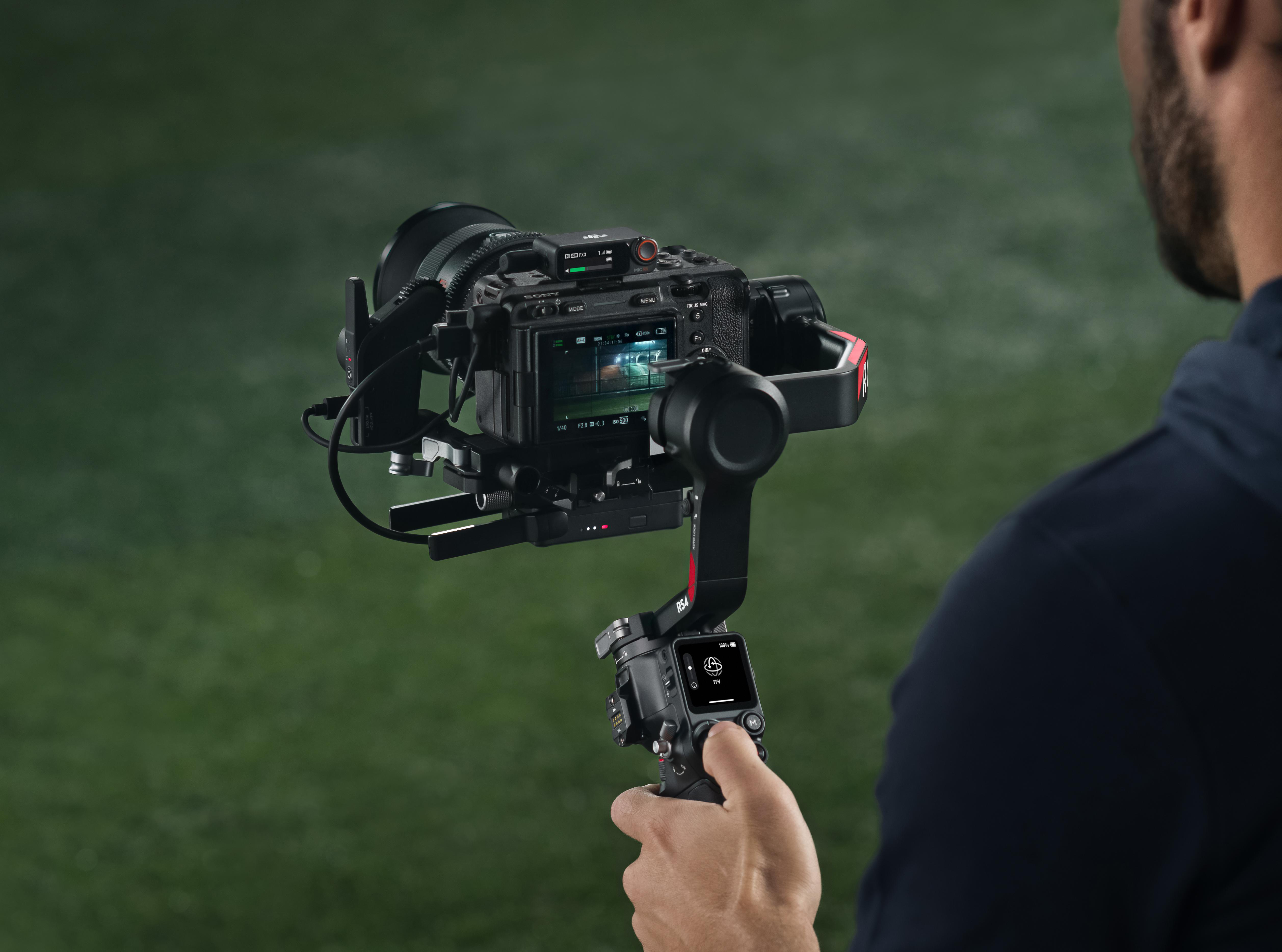 Eine Person hält eine Kamera auf einem Gimbal. Die Kamera ist schwarz, und der Hintergrund ist ein grünes Feld.