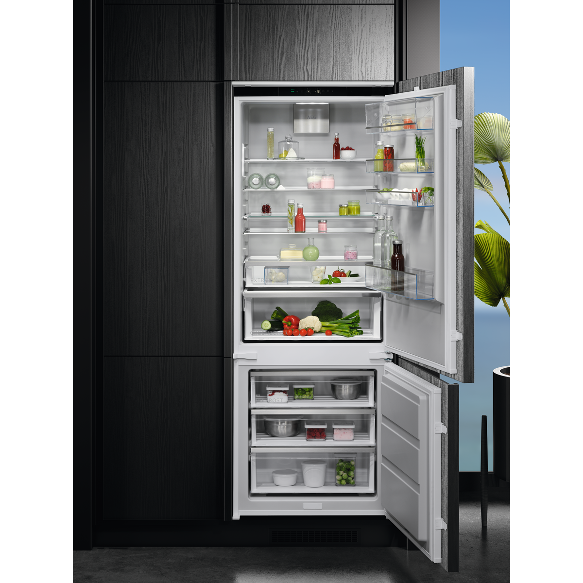 Refrigerador abierto con estantes llenos de comida, con armarios negros al fondo.