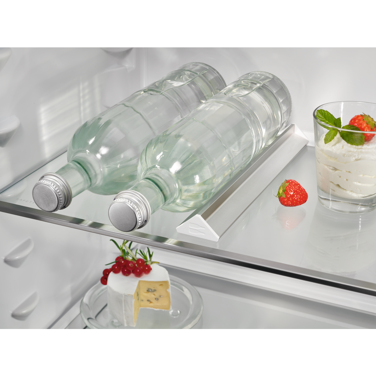 Estante de refrigerador con botellas de agua, una fresa y un postre.