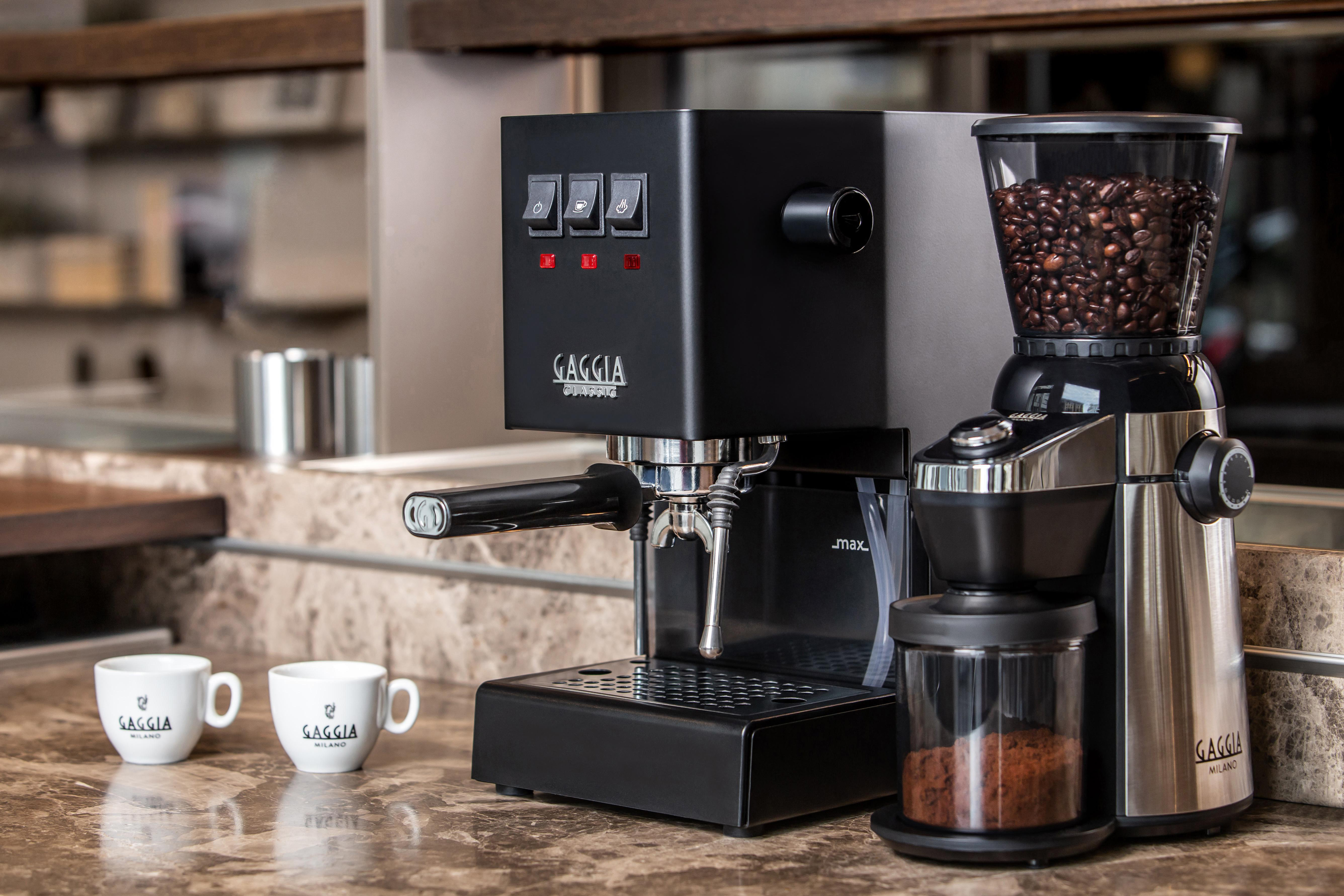 Schwarze Espressomaschine und Mühle, Kaffeebohnen, zwei Tassen auf Theke.