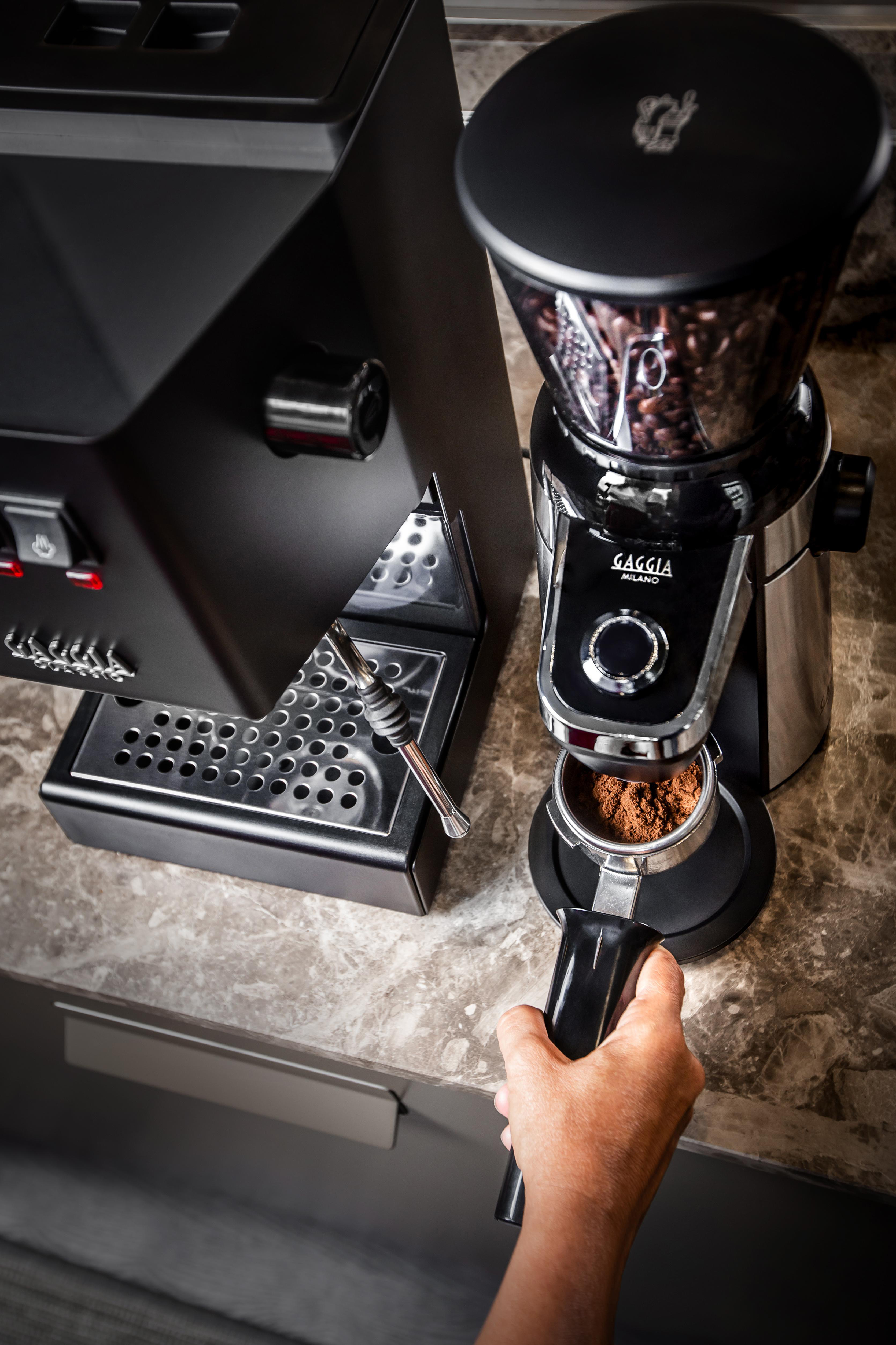 Eine Person hält eine Kaffeemühle neben einer Espressomaschine.
