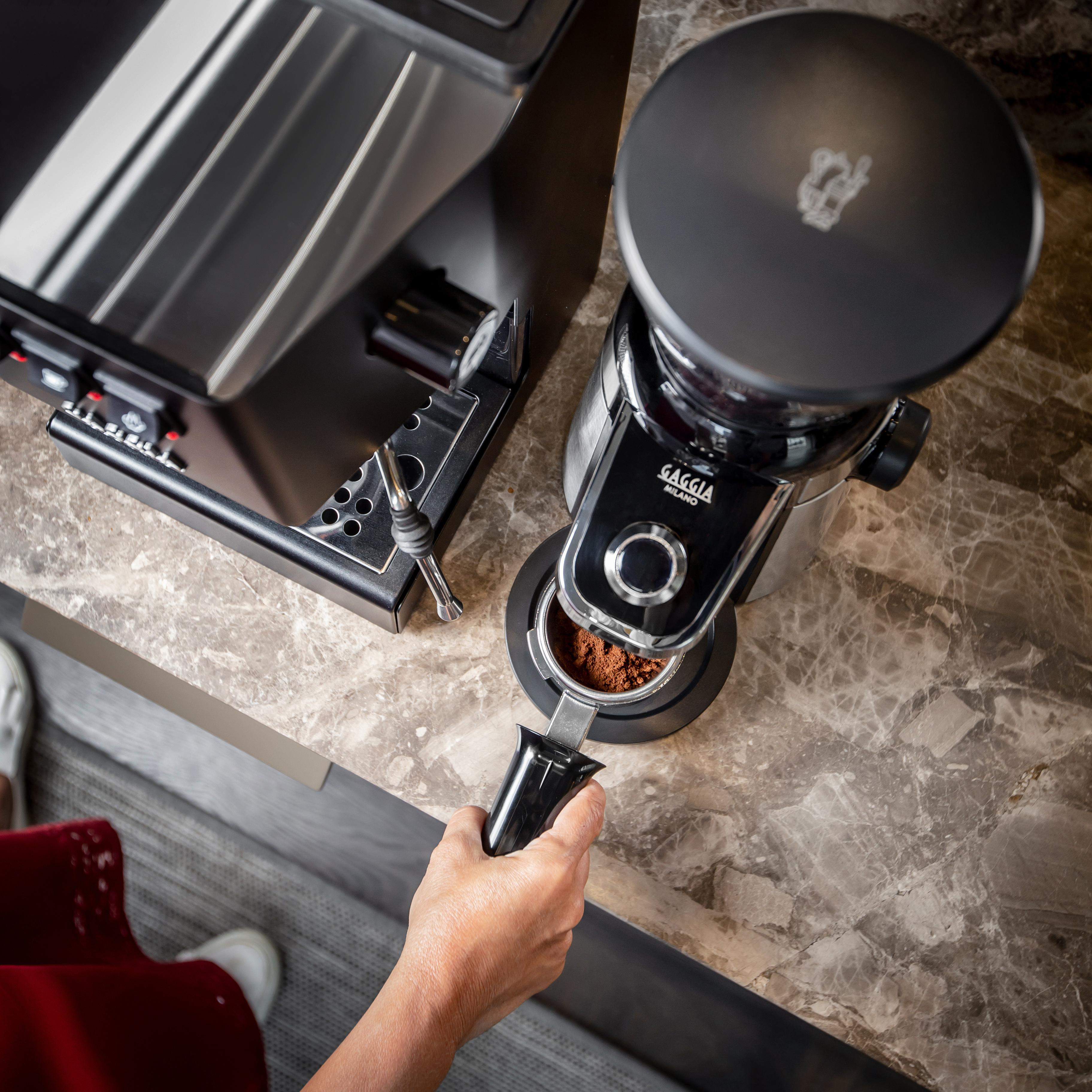 Eine Kaffeemaschine mit Mahlwerk wird benutzt. Eine Hand hält den Siebträger.