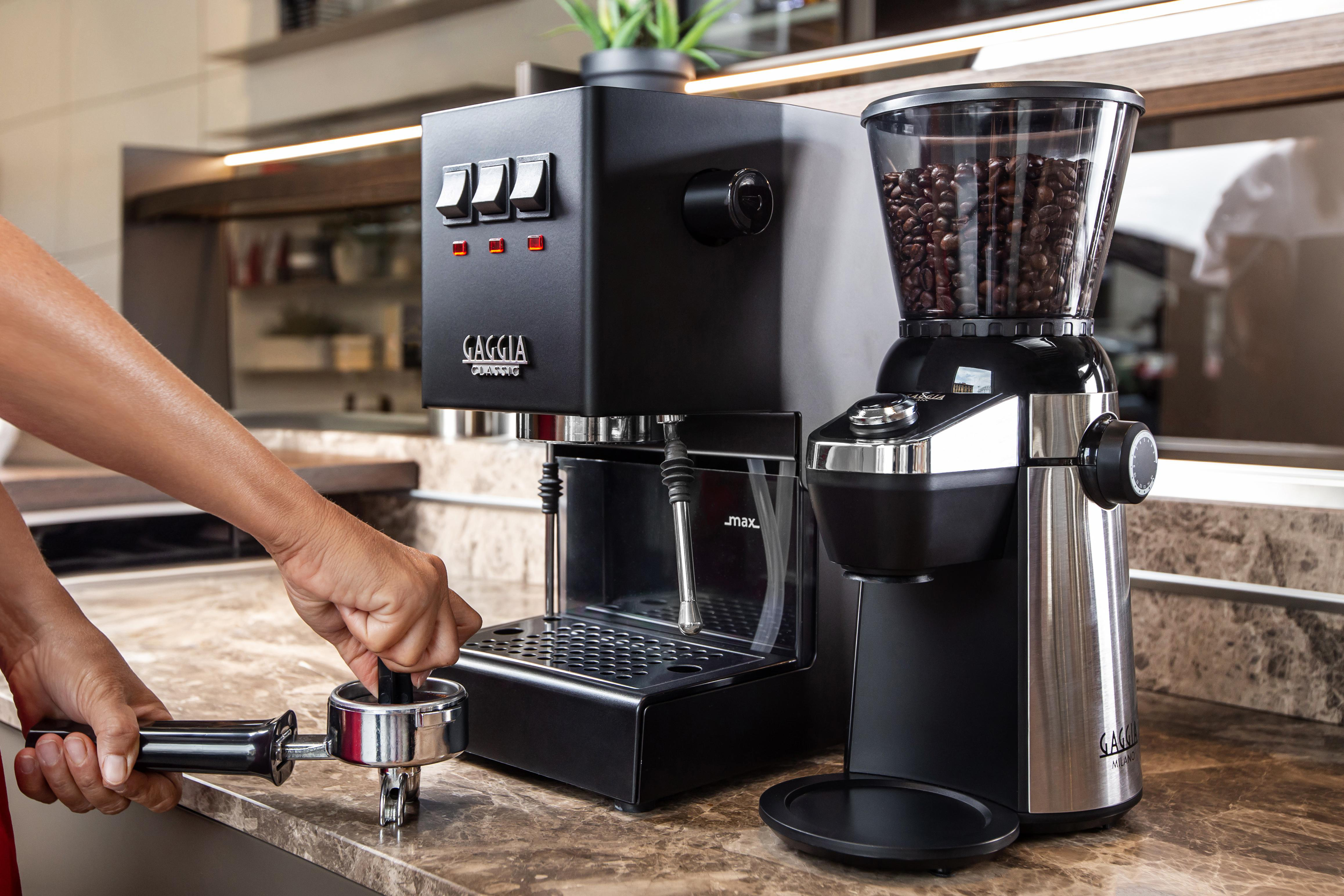 Espressomaschine und Kaffeemühle auf einer Theke, mit einer Person, die einen Siebträger benutzt.
