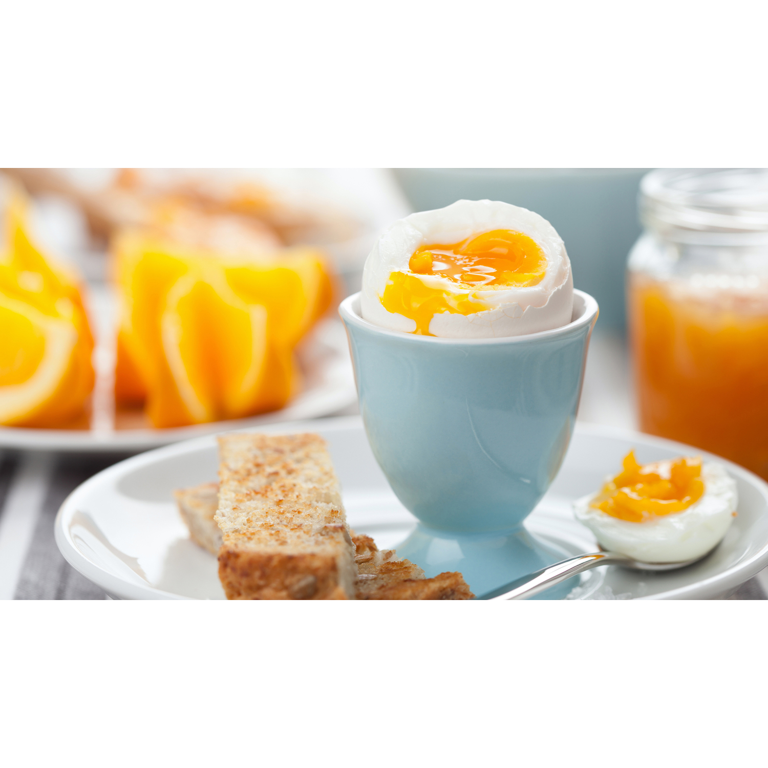 Zachtgekookt ei in een blauwe eierdop, met toast en sinaasappelschijfjes. Een lepel ligt bij het ei.
