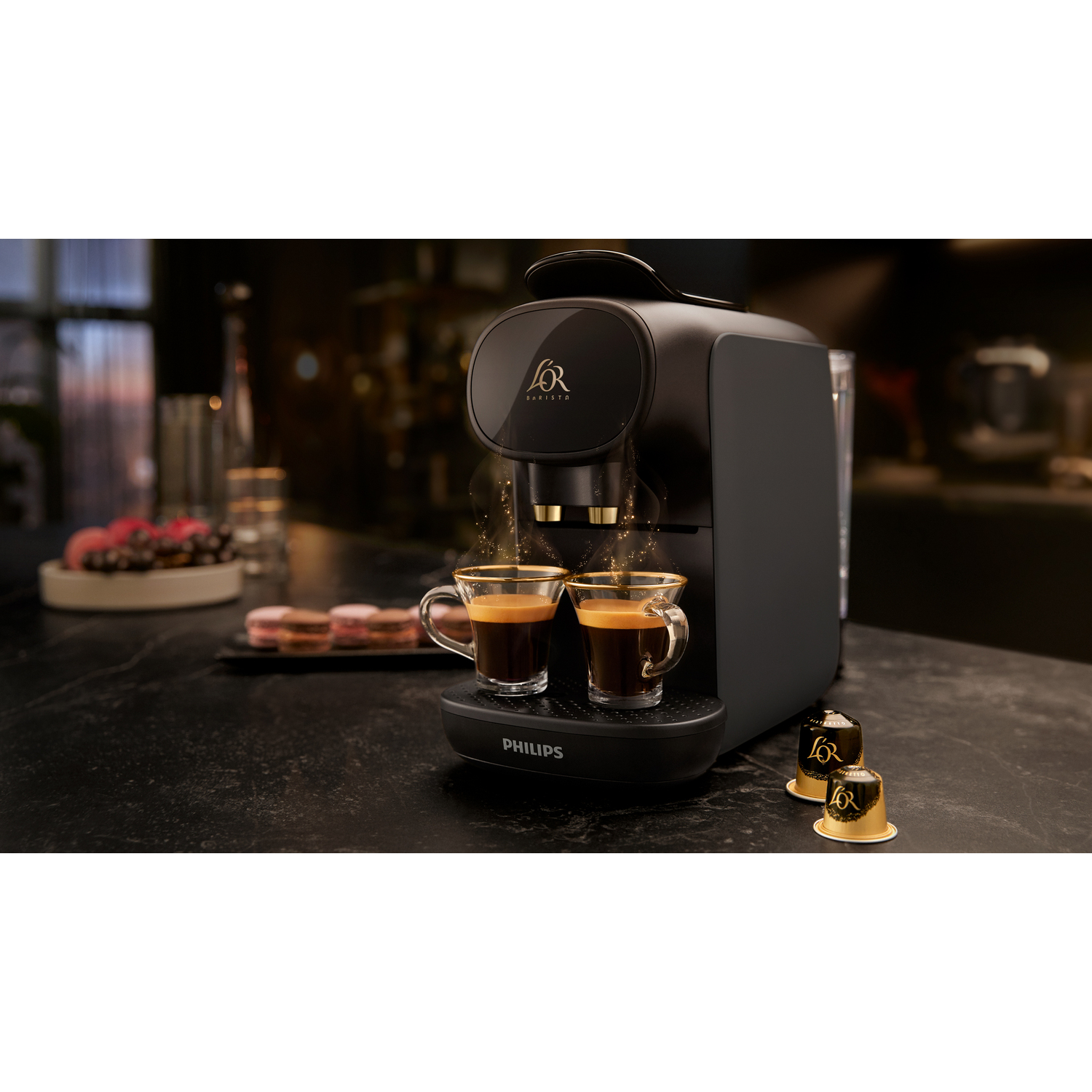 Koffiezetapparaat, twee kopjes koffie en capsules op een donkere ondergrond.