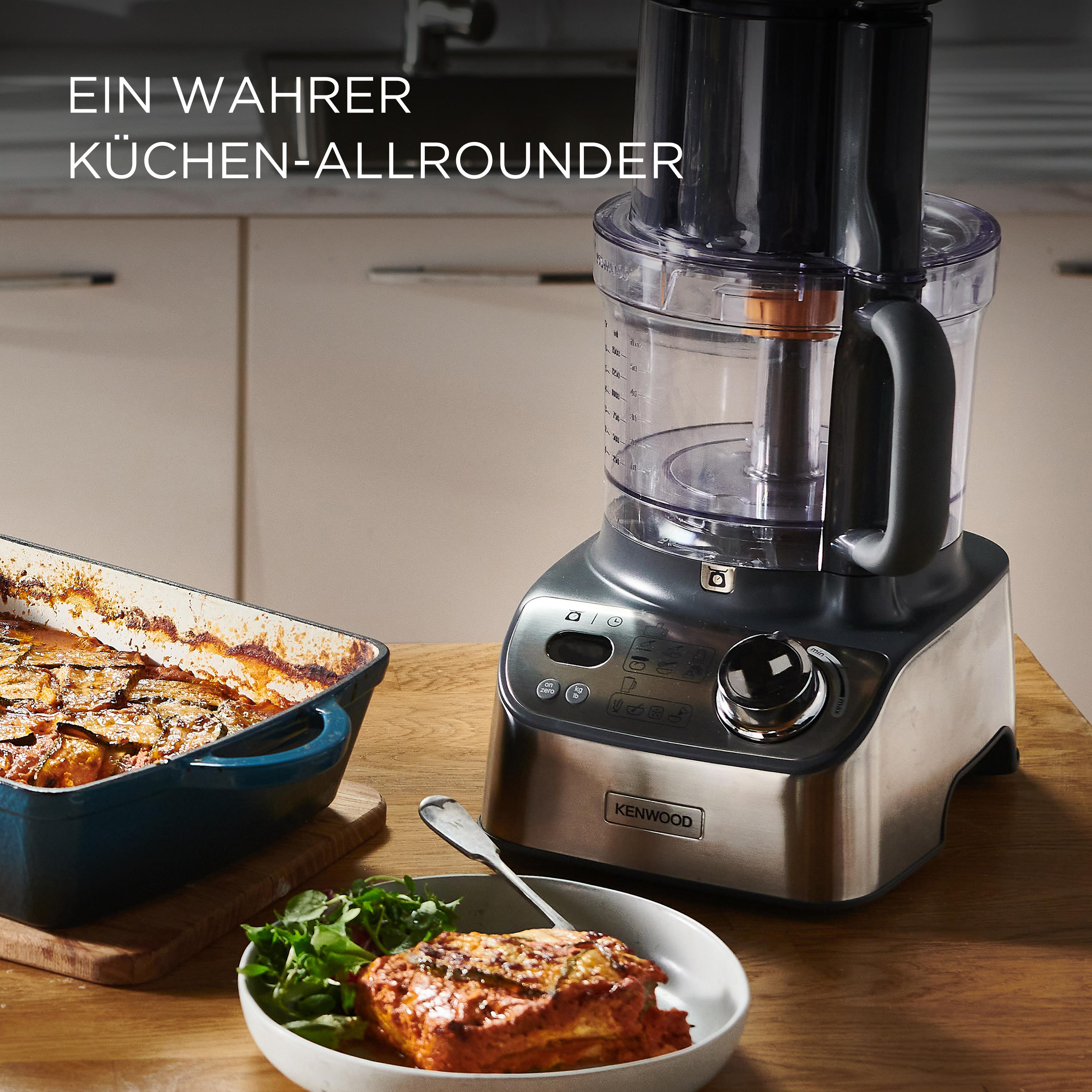 Ein Kenwood-Küchengerät steht auf einem Holztisch. Auflauf und Schüssel mit Essen sind im Vordergrund.