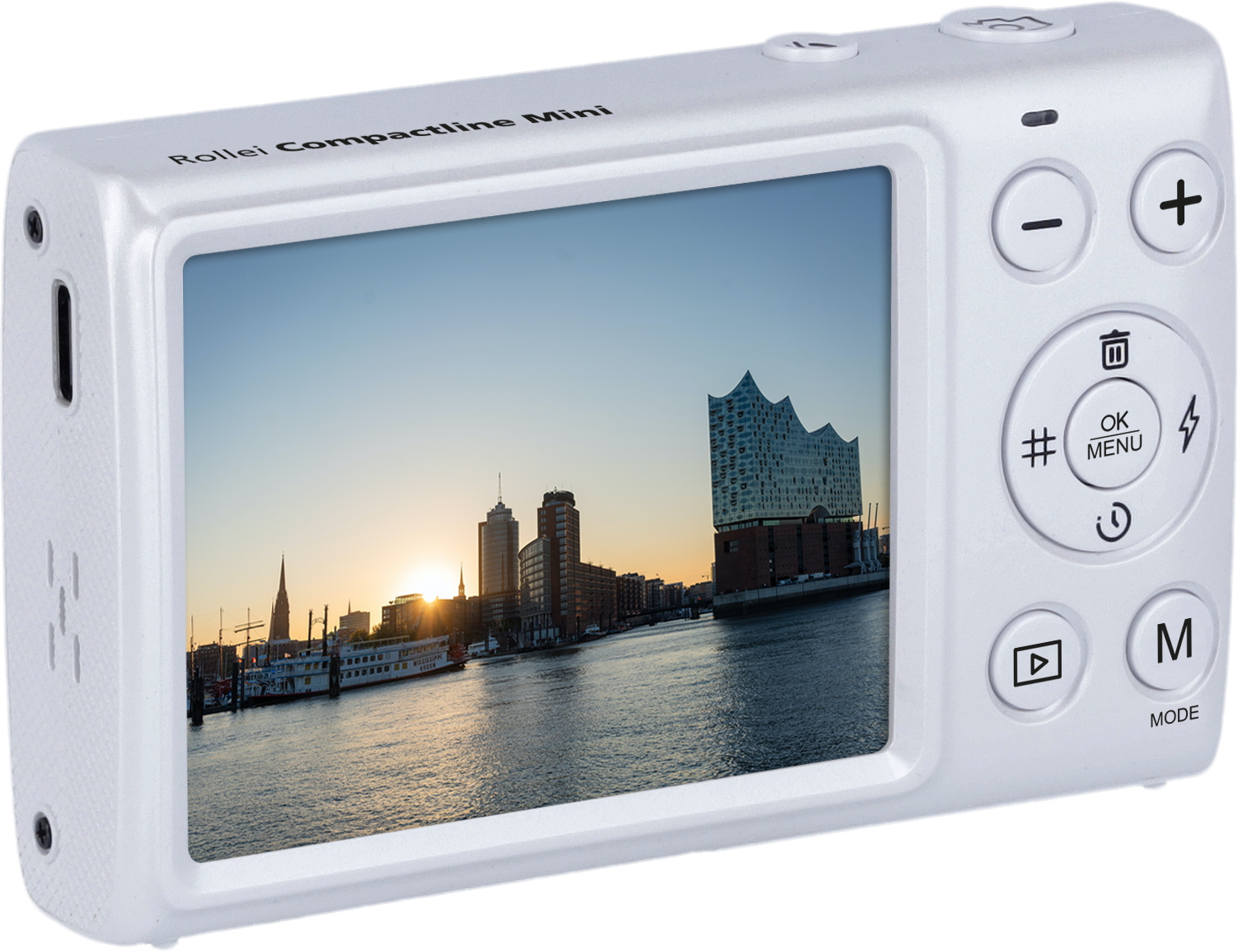 Eine weiße Digitalkamera zeigt eine Stadtsilhouette auf ihrem Bildschirm; die Sonne geht über dem Wasser unter.