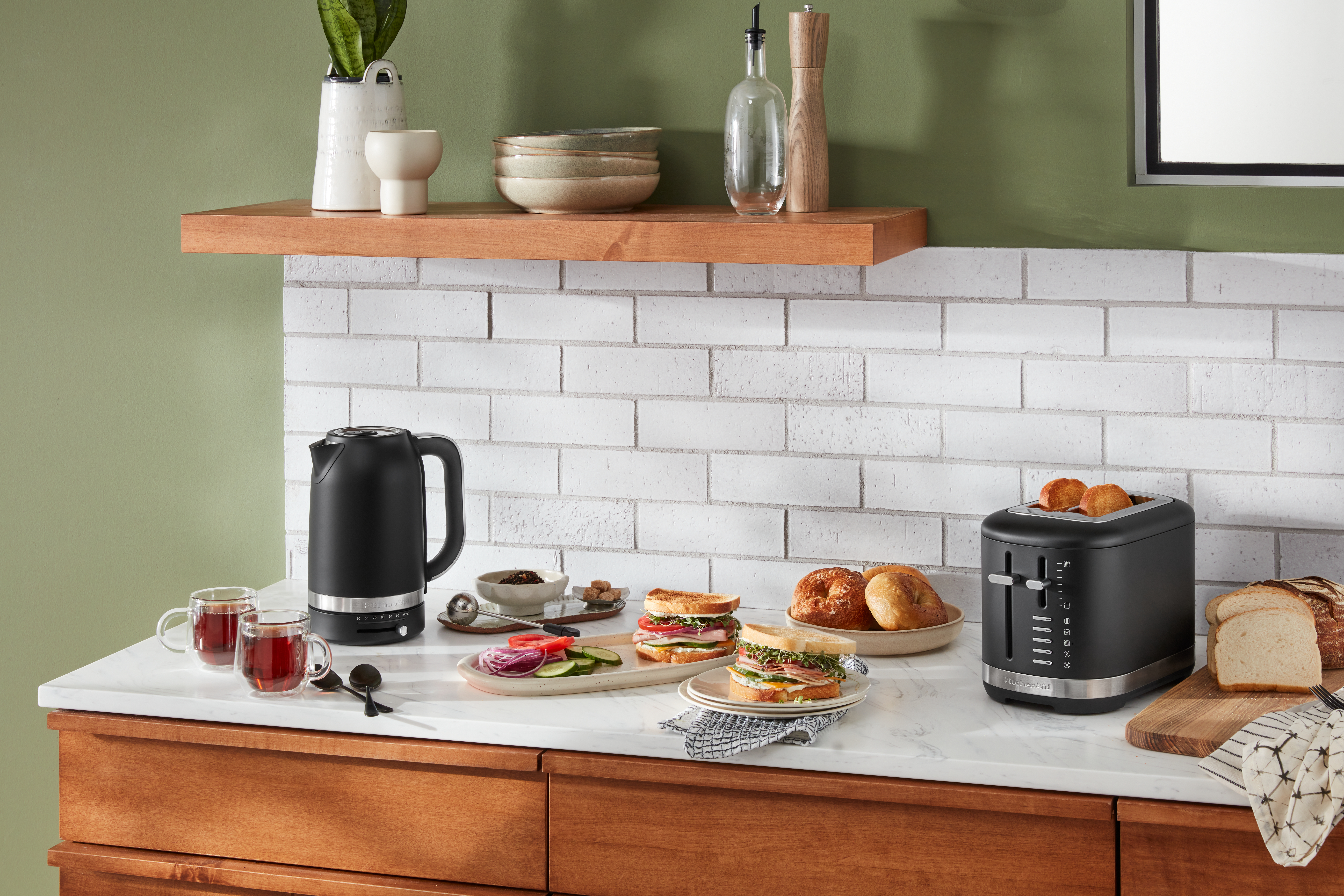 Küchentheke mit Lebensmitteln, einem schwarzen Wasserkocher und einem Toaster. Der Hintergrund ist eine Wand.