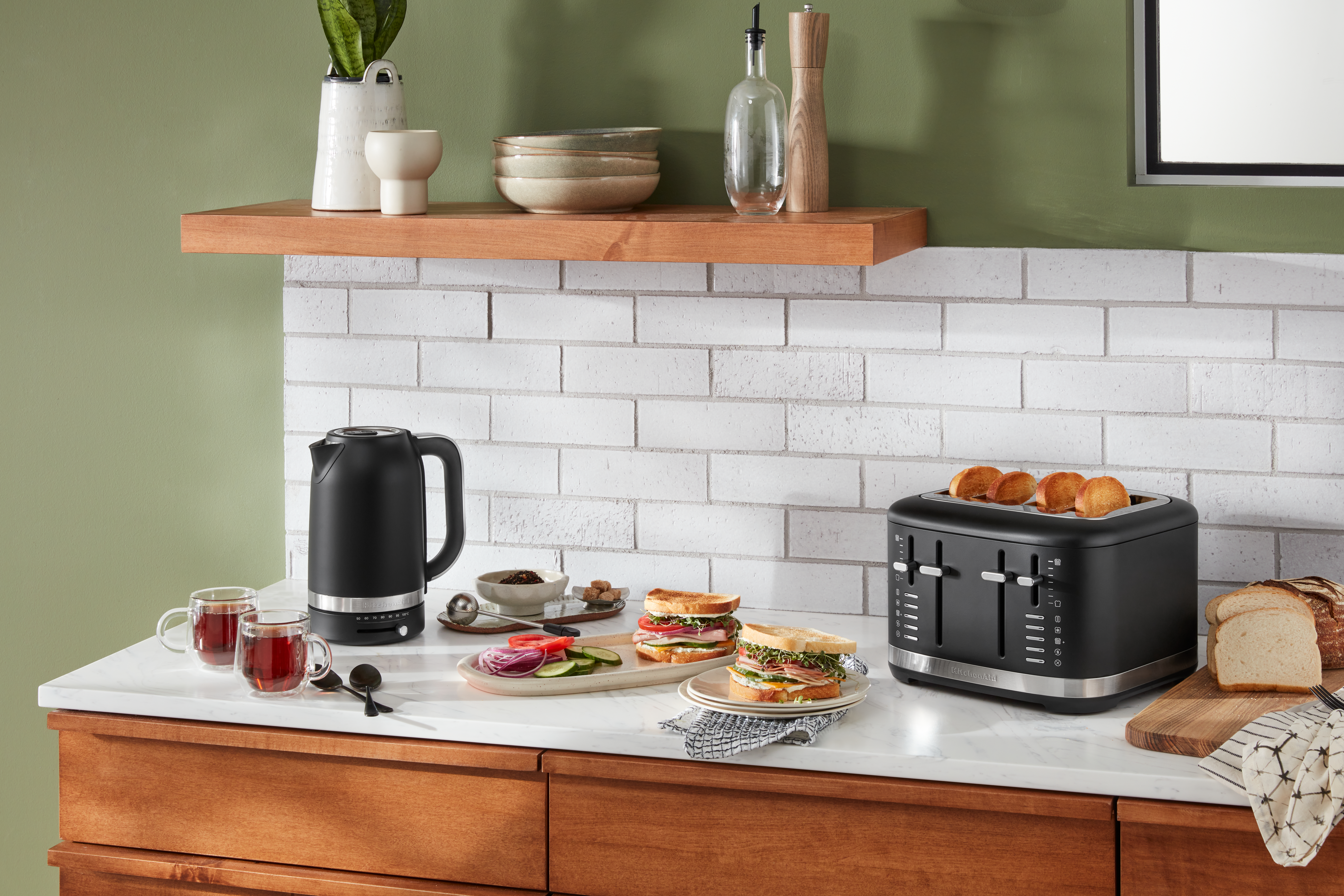 Eine Küchenszene mit einem schwarzen Wasserkocher, Sandwiches und einem Toaster.