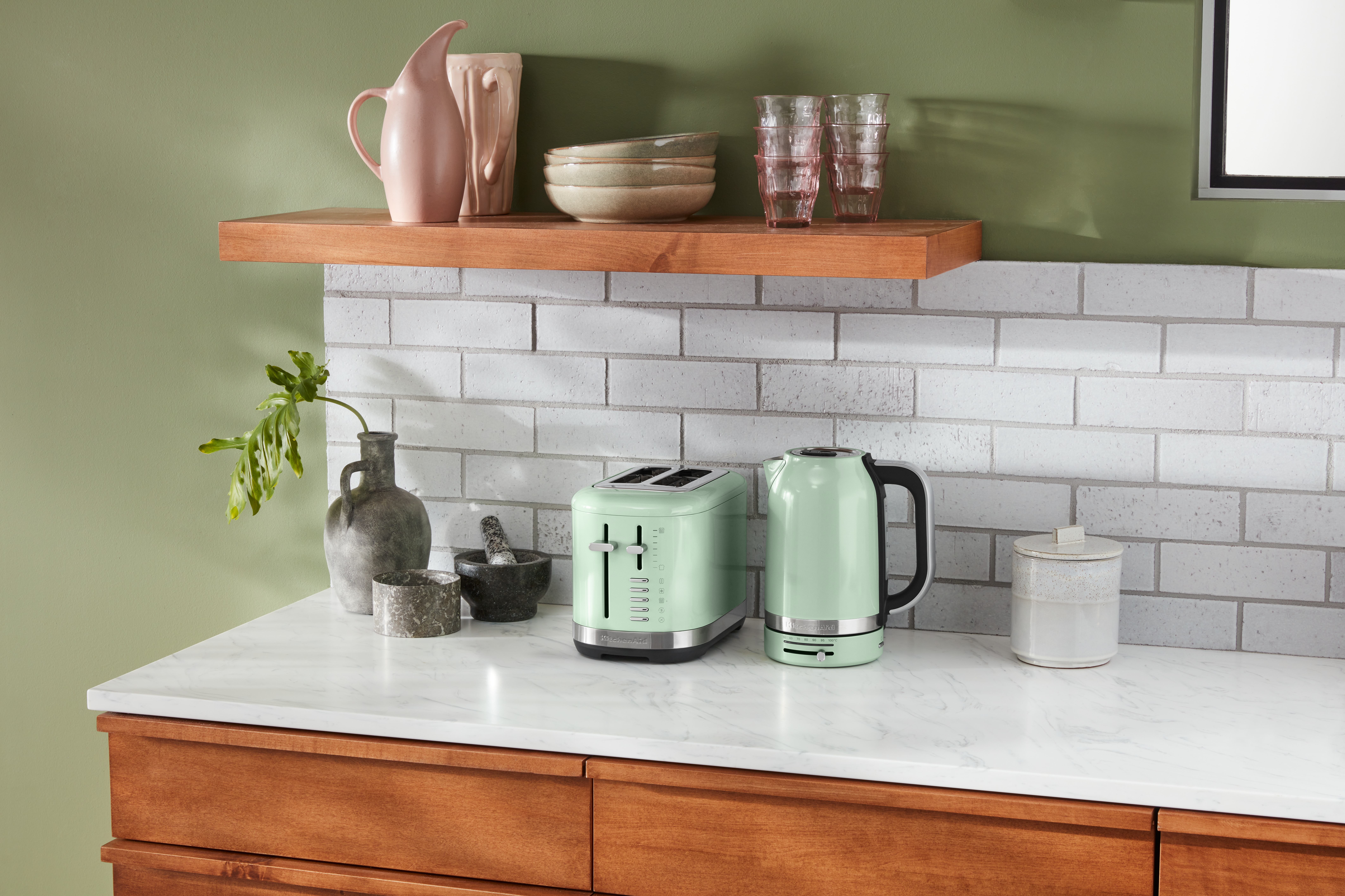 Küche mit Arbeitsplatte, Toaster und Wasserkocher. Darüber ein Regal mit Schalen und einem rosa Krug.