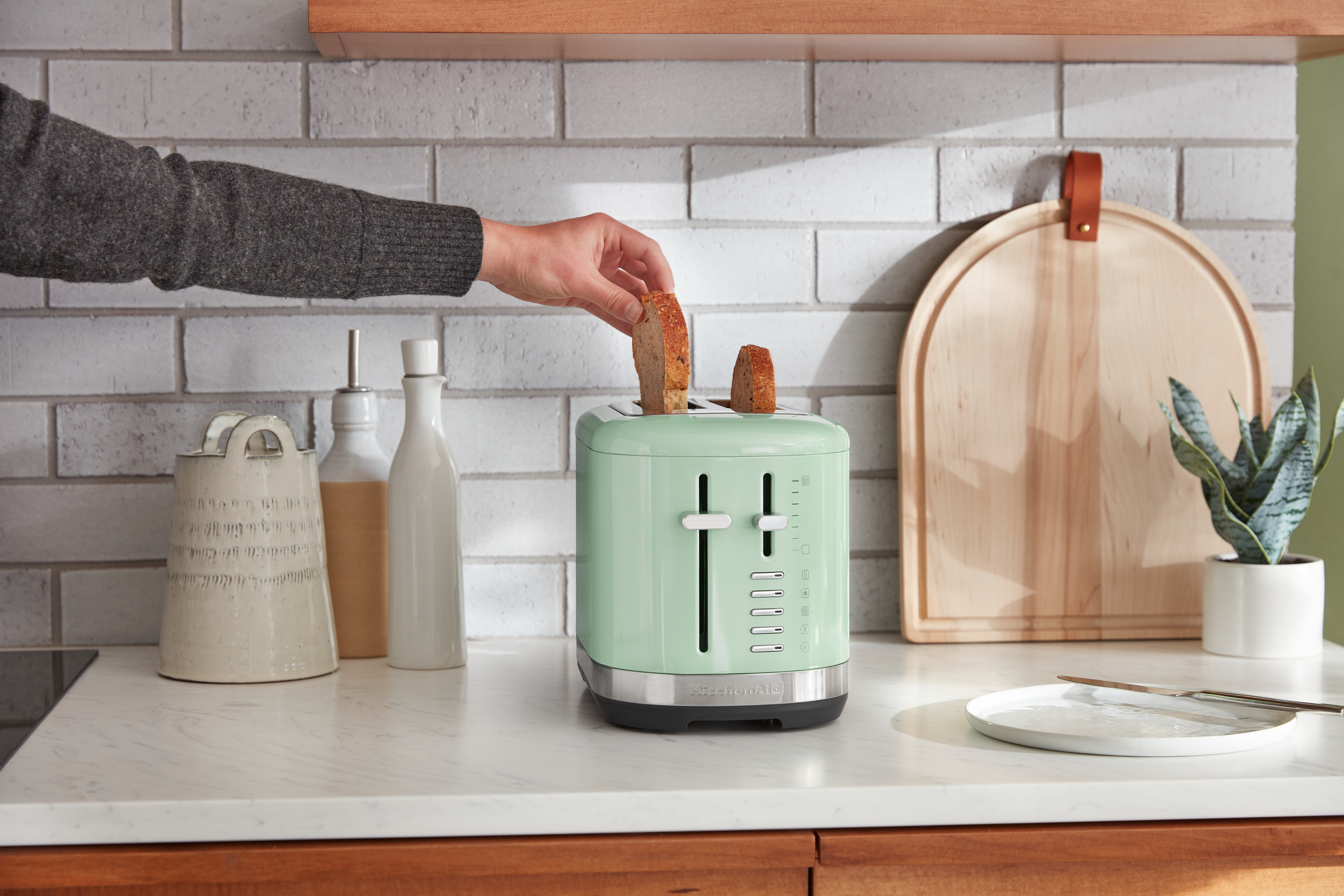 Eine Person nimmt ein Toastbrot aus einem grünen Toaster.