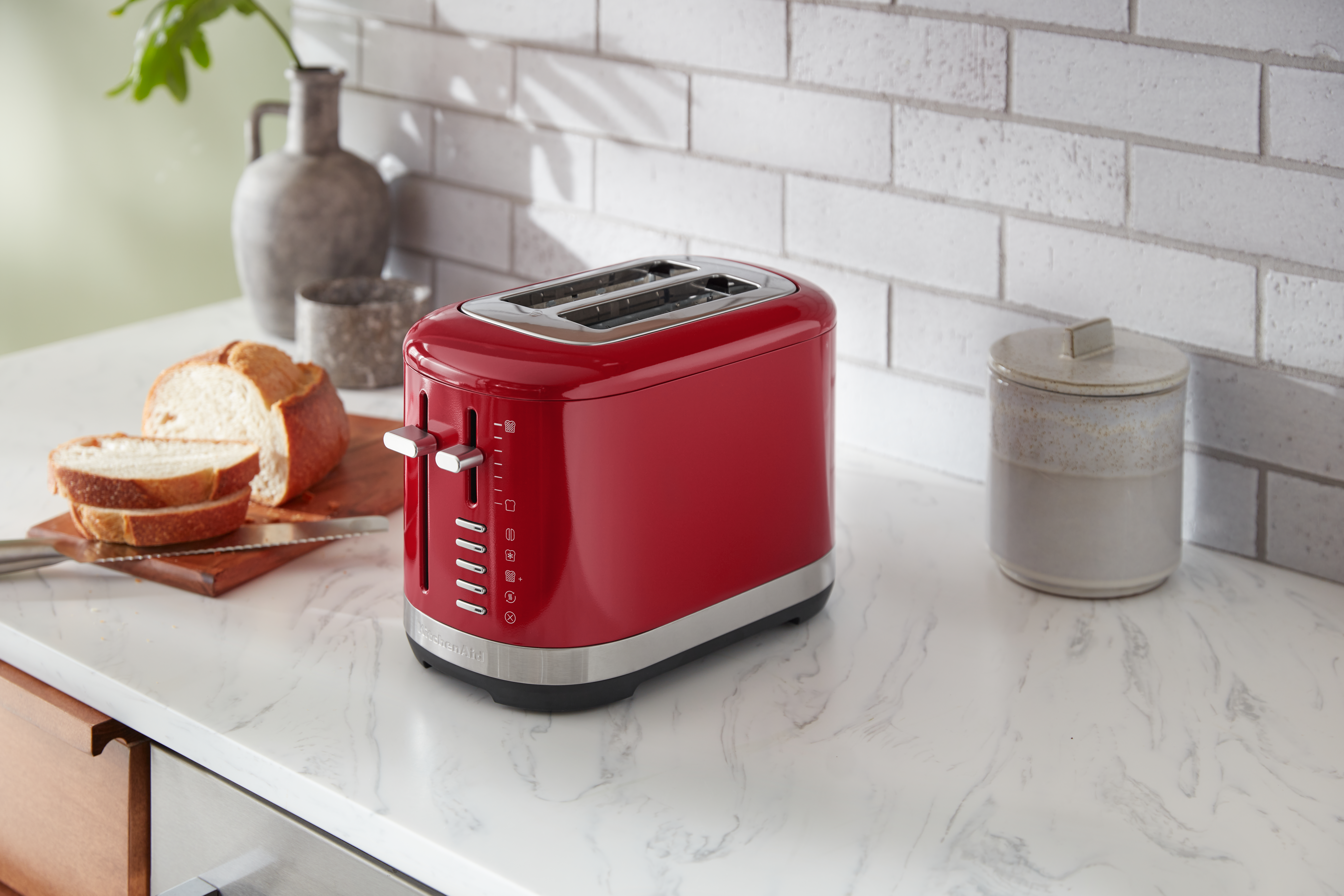 Roter Toaster mit Brot und einem Glas auf einer weißen Arbeitsplatte.