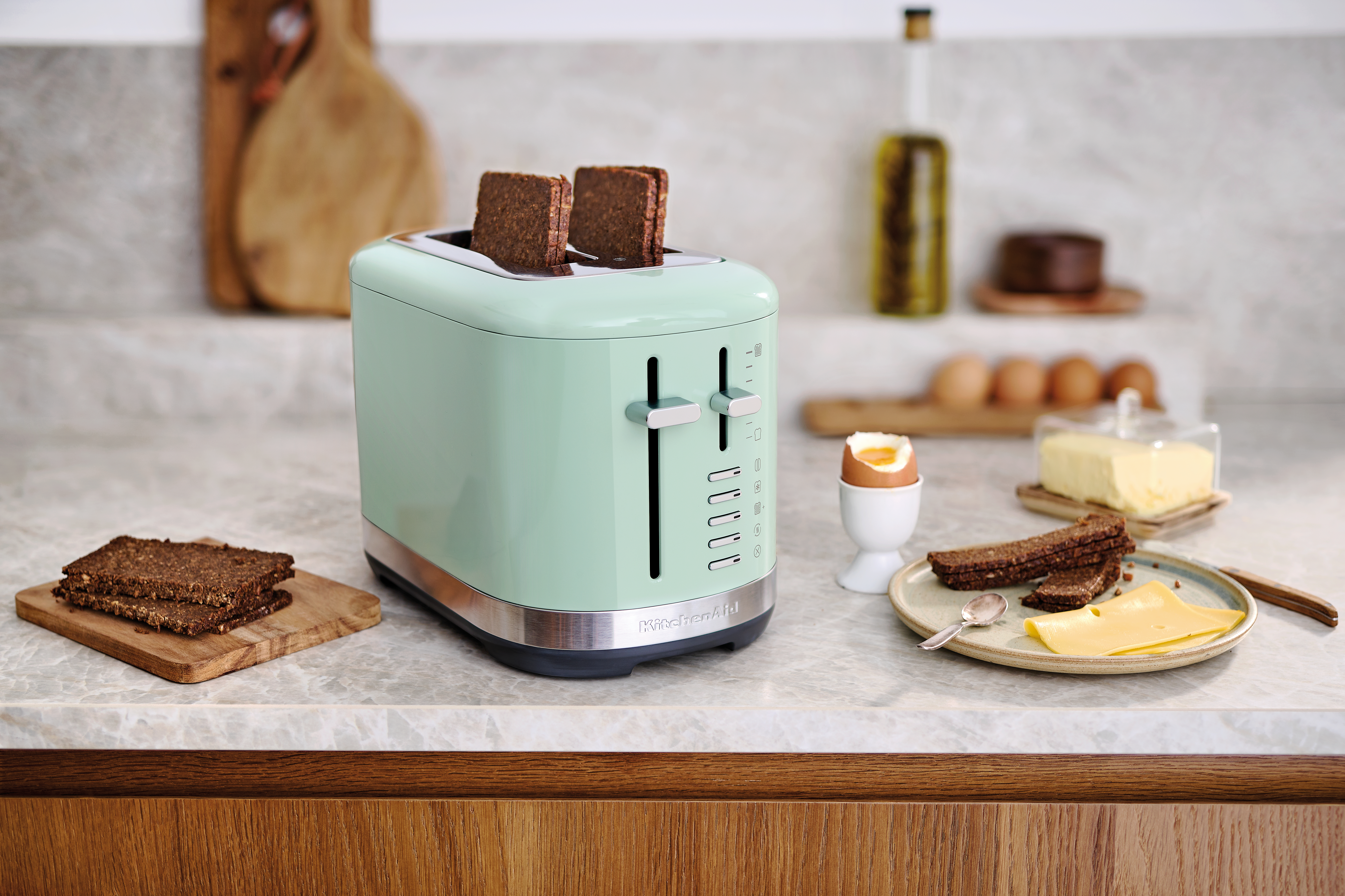 Minzgrüner Toaster mit Toast und Frühstücksartikeln auf Marmoroberfläche.