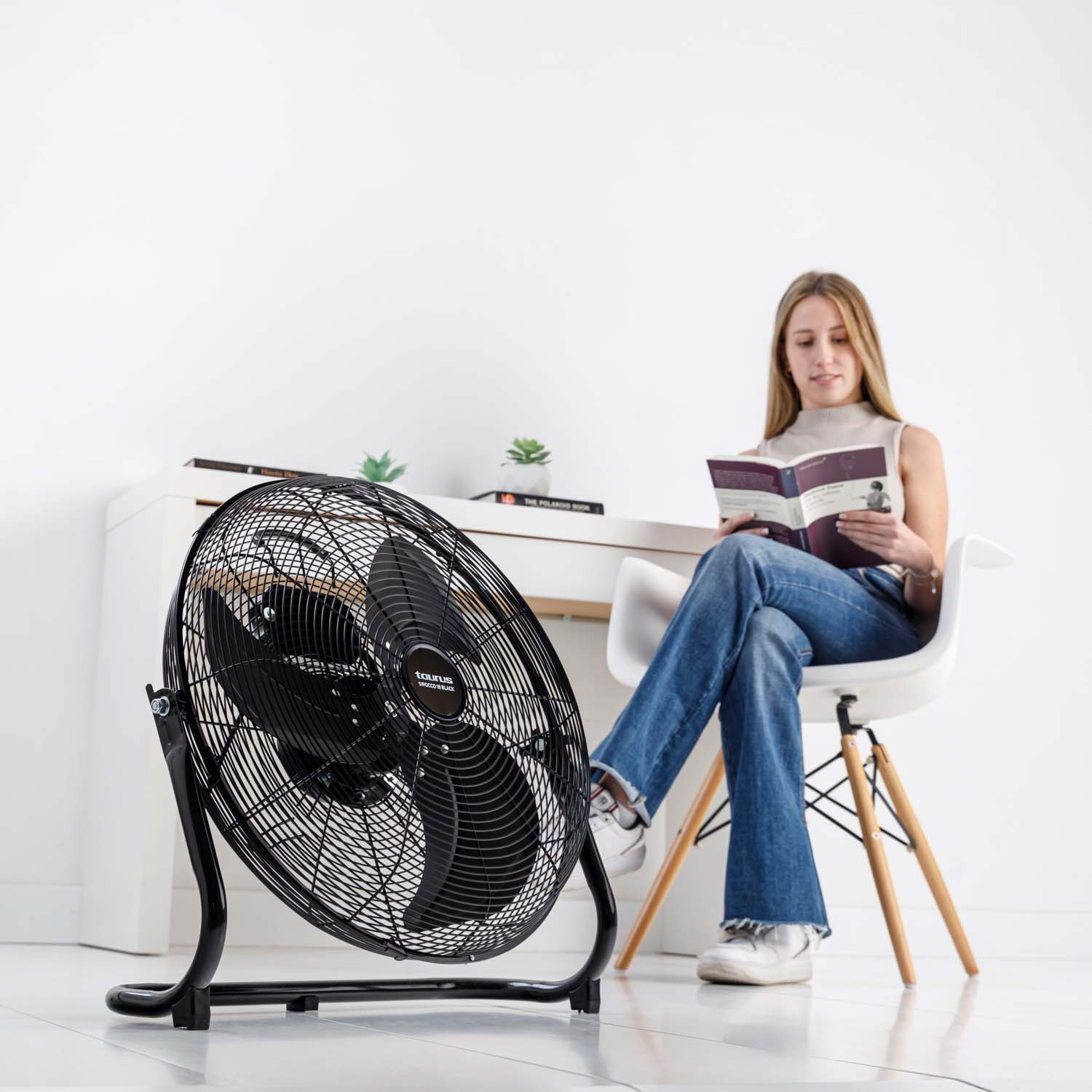 Una mujer leyendo un libro junto a un ventilador negro, con un piano al fondo.