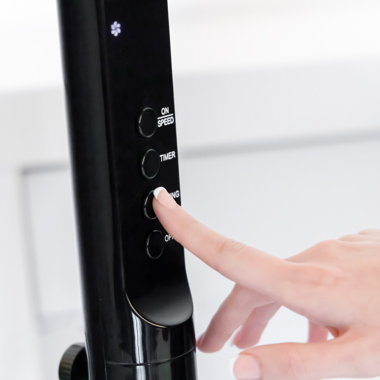 Una mano presiona el botón 'temporizador' en un ventilador negro de aspecto moderno con una pantalla digital.