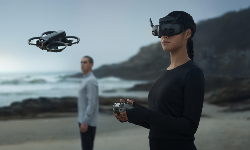 Osoba z goglami do drona, dron w powietrzu, inna osoba na plaży.