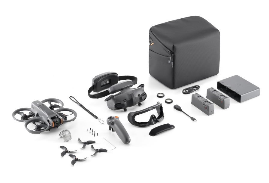 Dron, gogle, kontroler, torba, baterie i akcesoria ułożone na białej powierzchni.