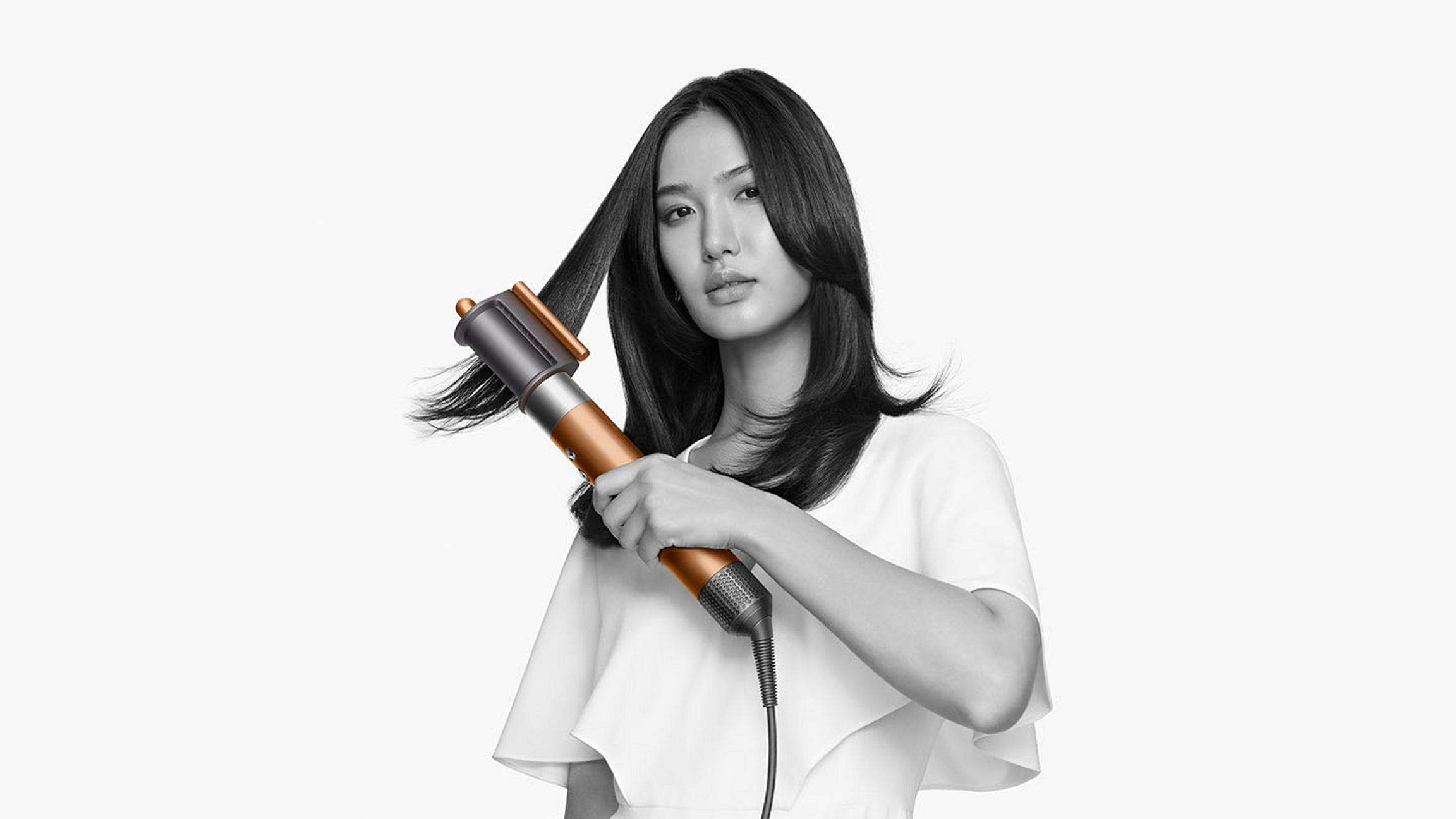 Frau stylt Haare mit Dyson Airwrap. Gold-graues Werkzeug. Weißer Hintergrund.